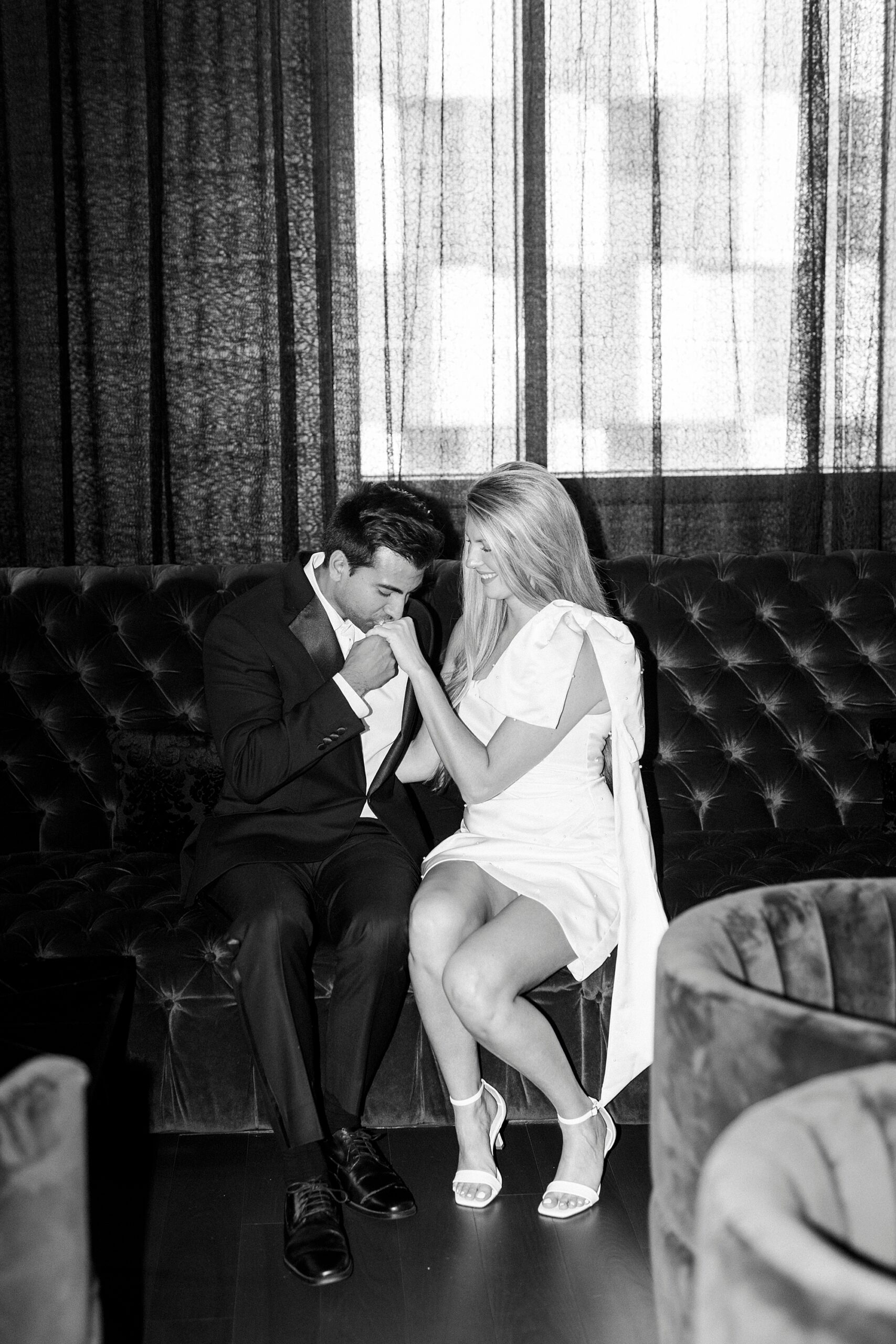 man kisses woman's hand sitting on leather couch in lobby of the Grand Bohemian Hotel in Charlotte NC