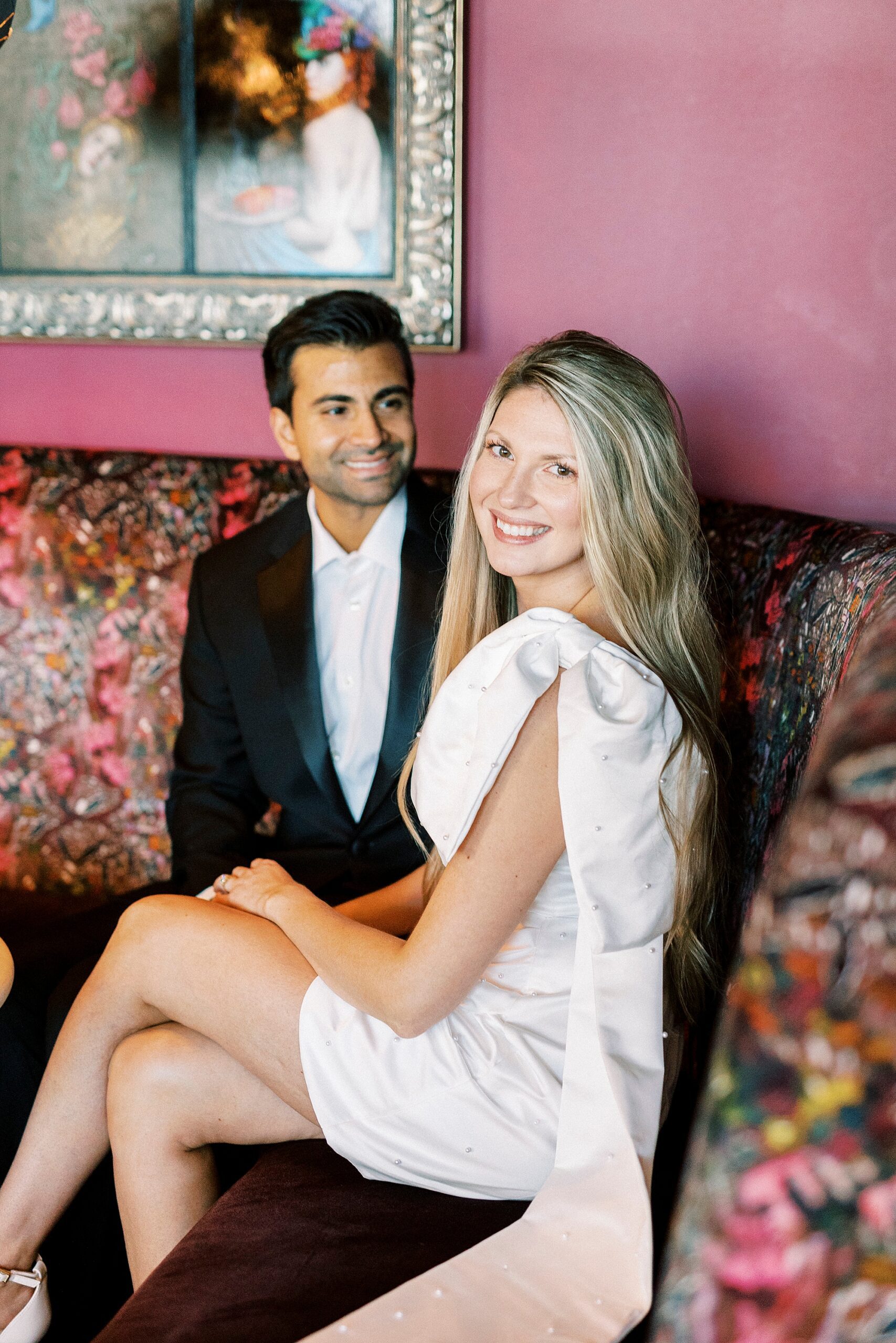 engaged couple sits on couch in front of pink wall at the Grand Bohemian Hotel in Charlotte NC