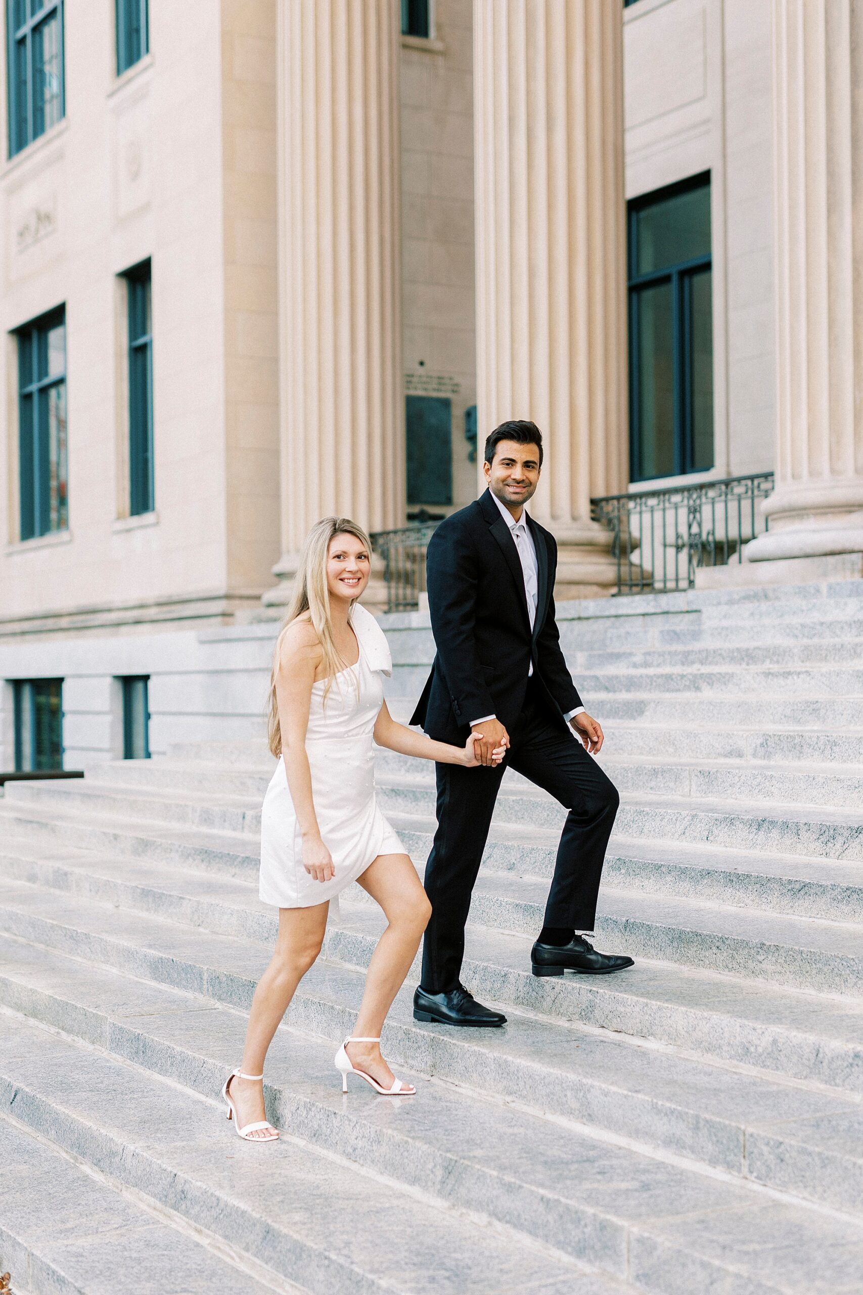 man and woman hold hands walking up the steps of building with columns in Charlotte NC