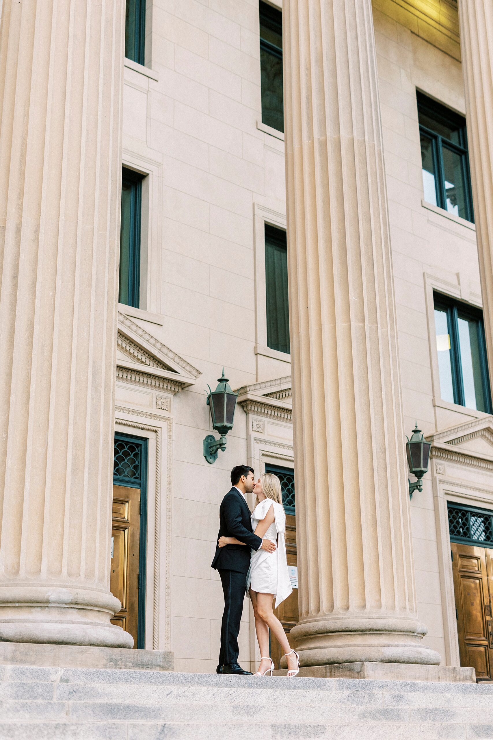 man and woman kiss on staircase between columns of Charlotte NC building 