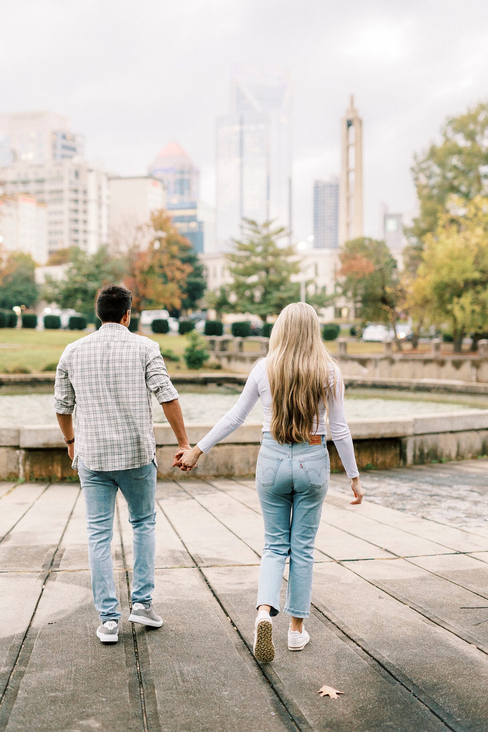 engaged couple hold hands walking towards fountain inside Marshall Park