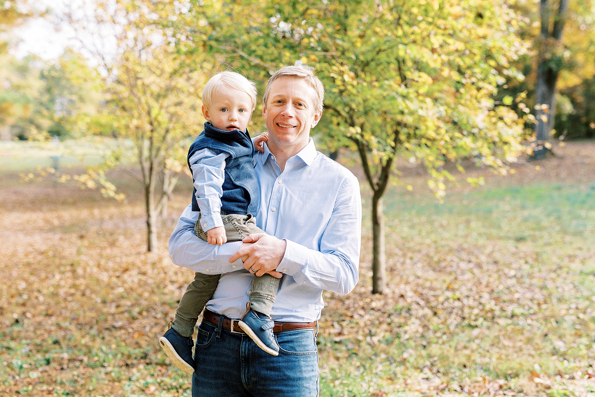 dad stands holding son on his hip during fall family photos