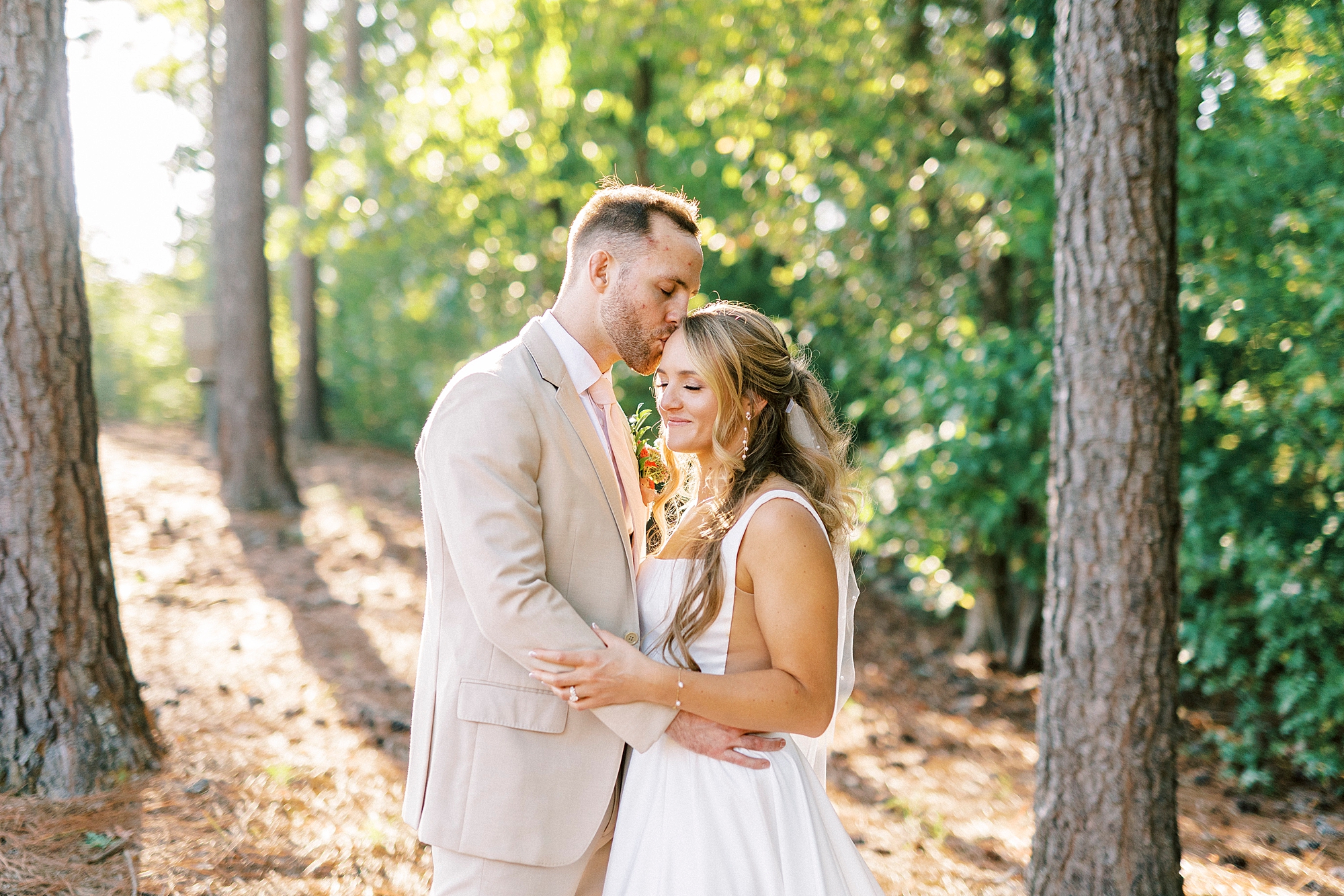 groom kisses bride between trees in backyard of NC home