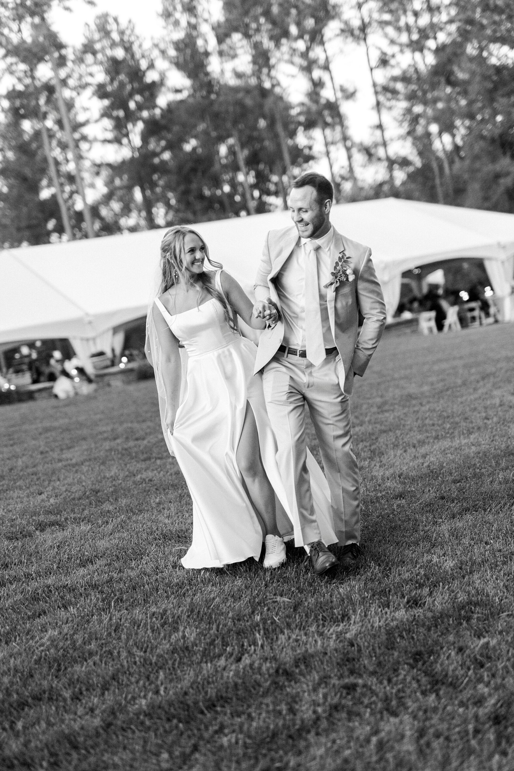 bride and groom bump hips walking away from tented reception 