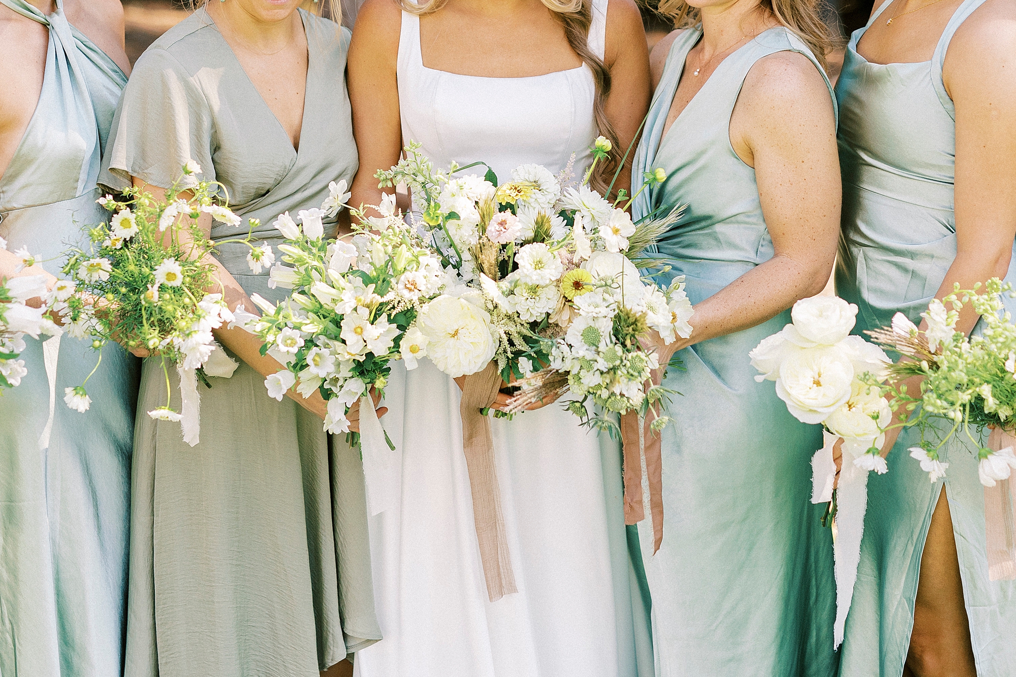 bridesmaids in mint gowns hold bouquets of white flowers with pink ribbons