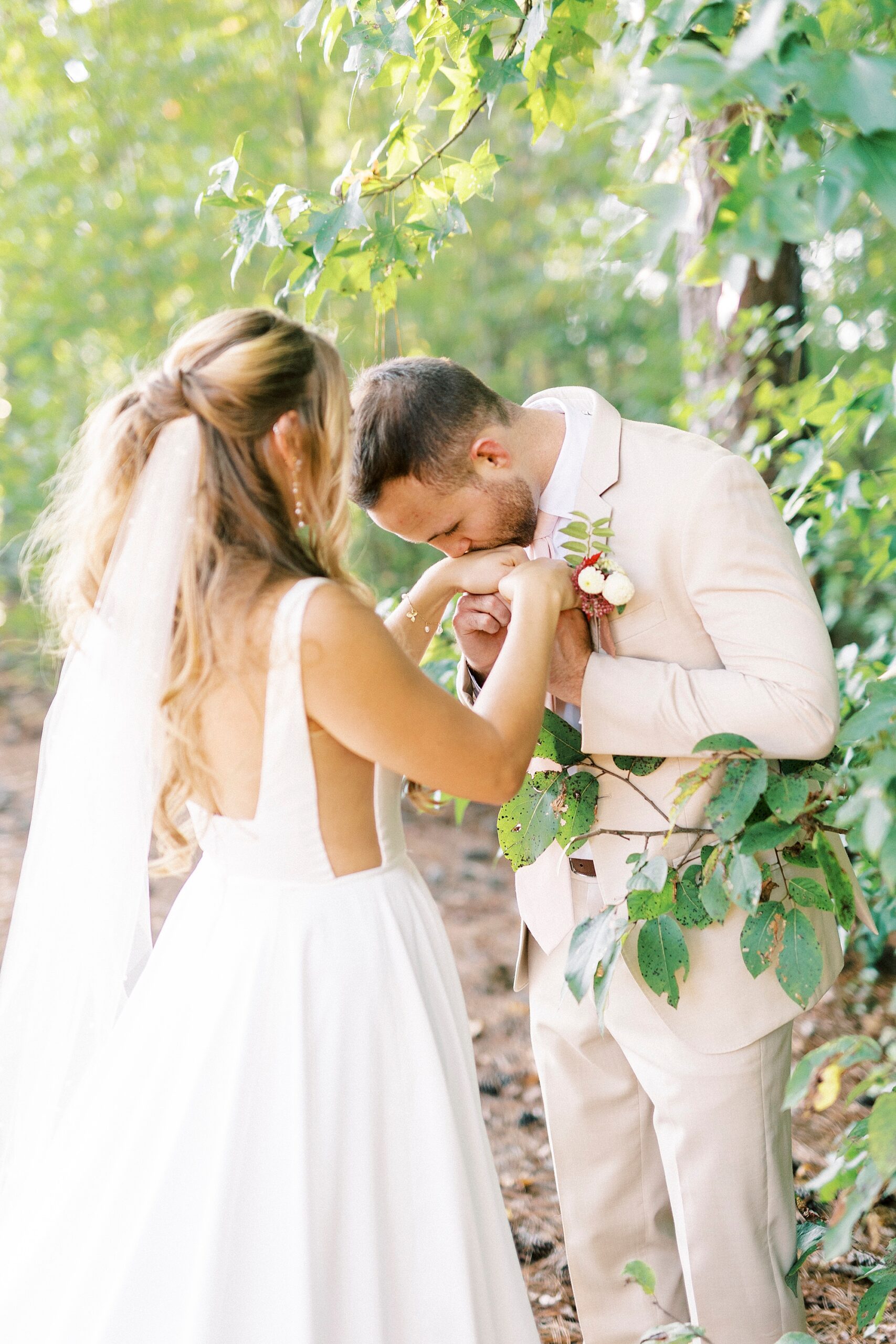 groom leans to kiss bride's hand during first look in woods