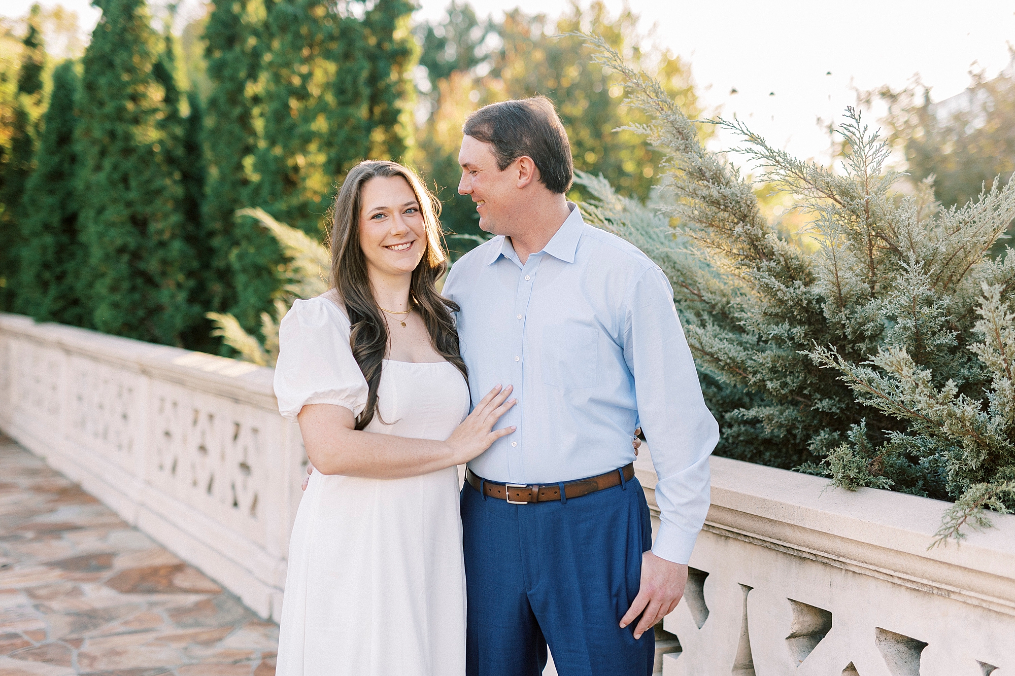 man smiles at fiancee in white dress on bridge in Midtown Park