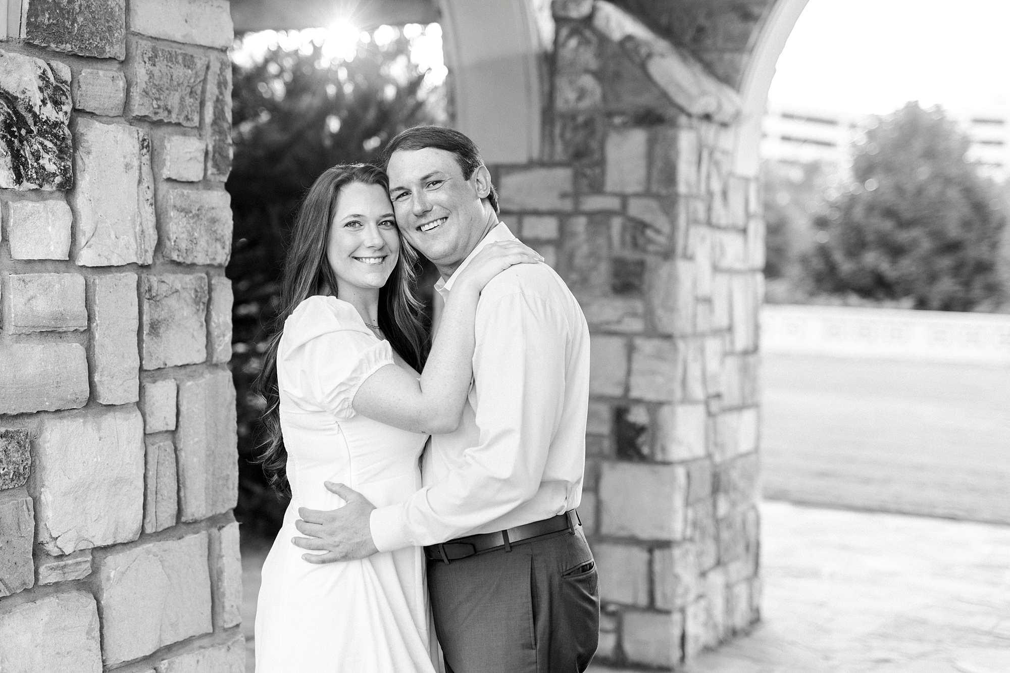 engaged couple hug by stone arches inside Midtown Park