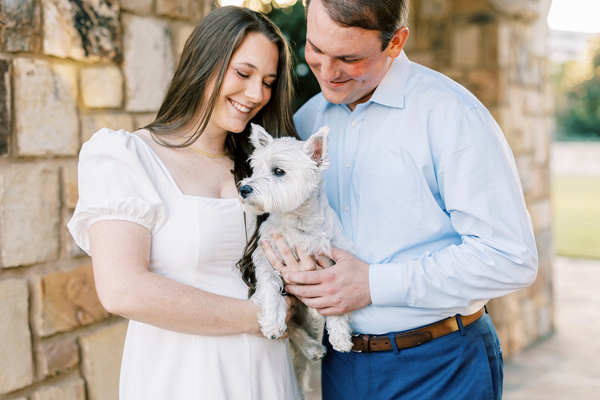 man and woman pose with small white dog during engagement photos in Midtown Park