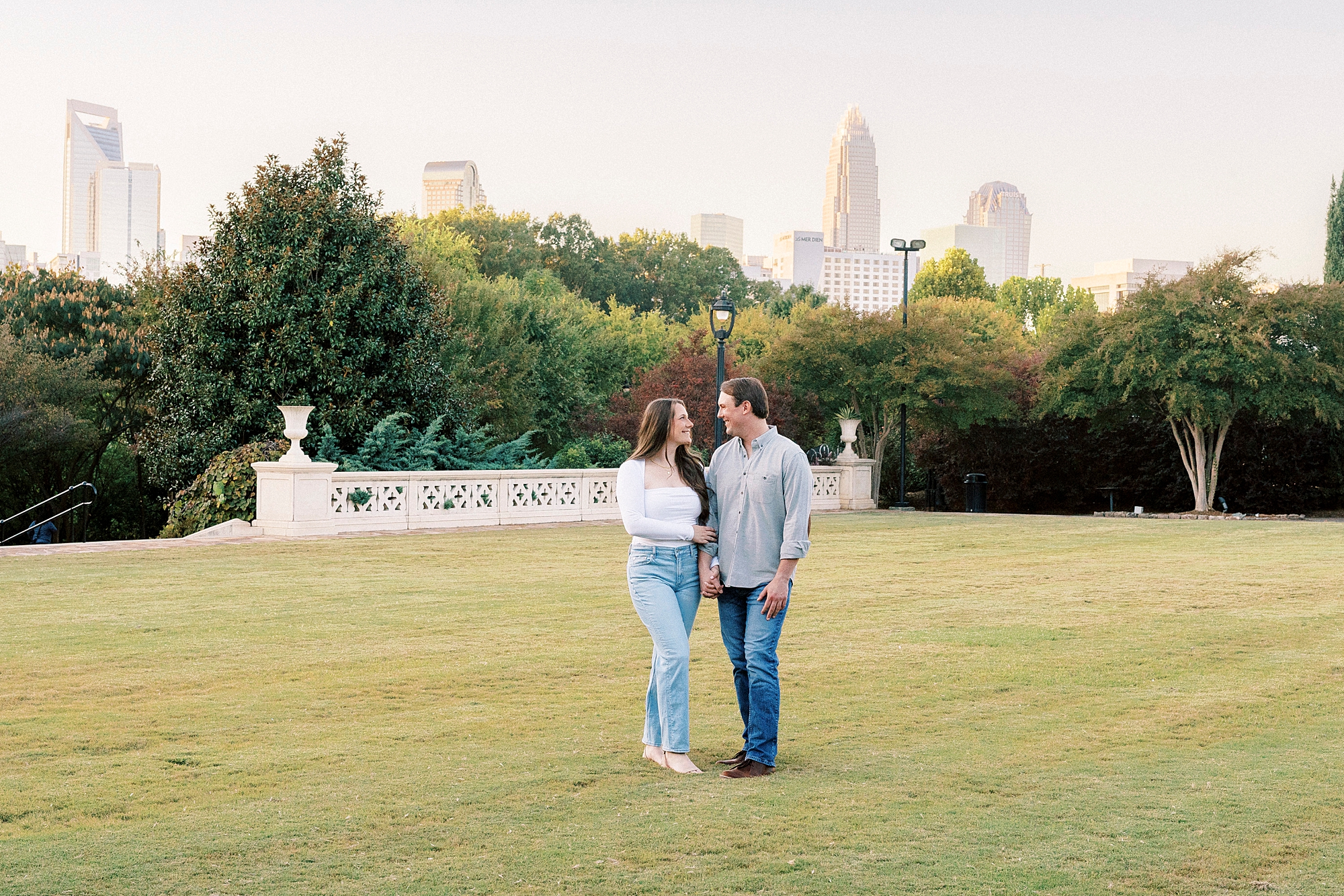 engaged couple stands on lawn inside park in Charlotte NC