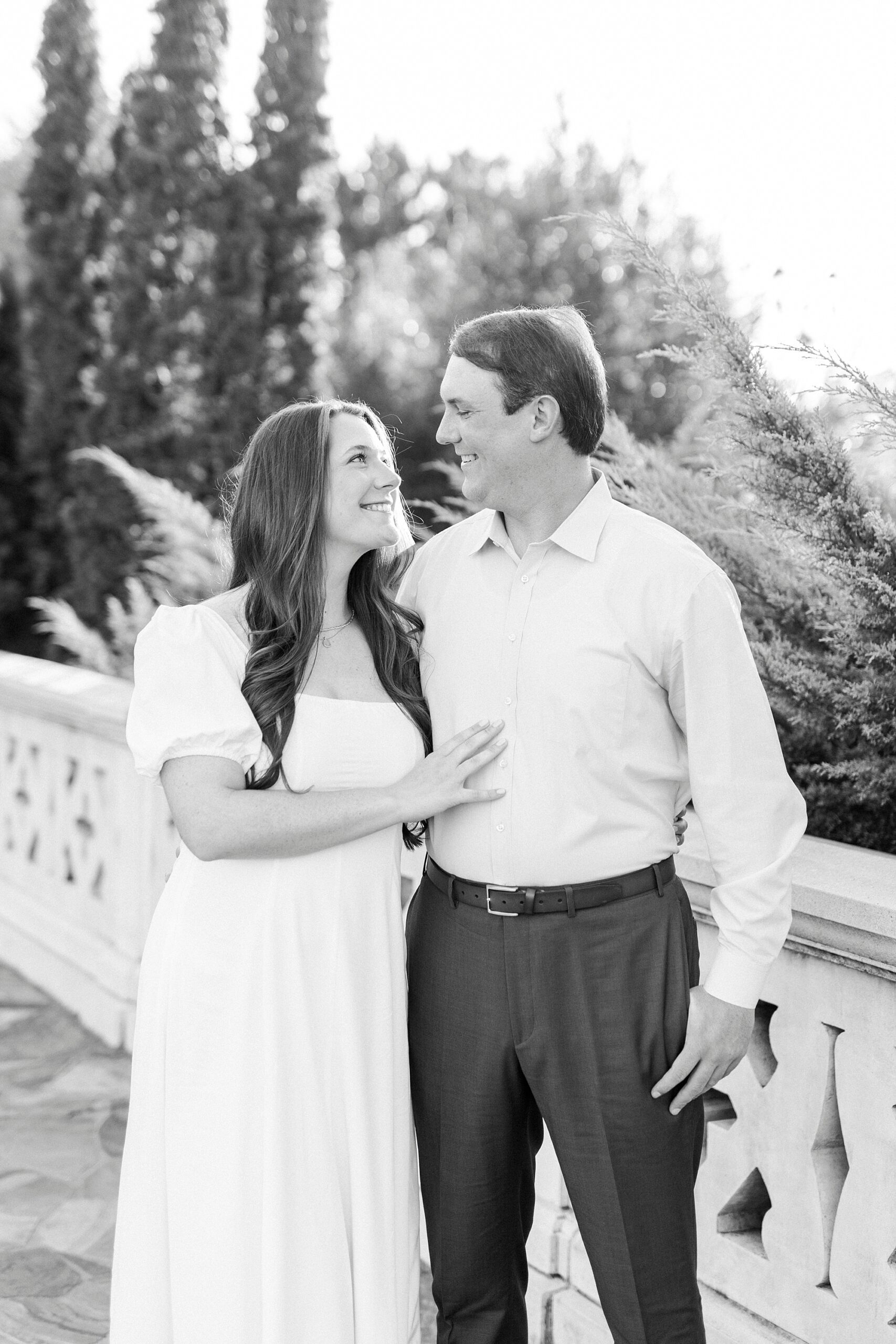 man smiles over at fiancee during engagement session on bridge inside Midtown Park