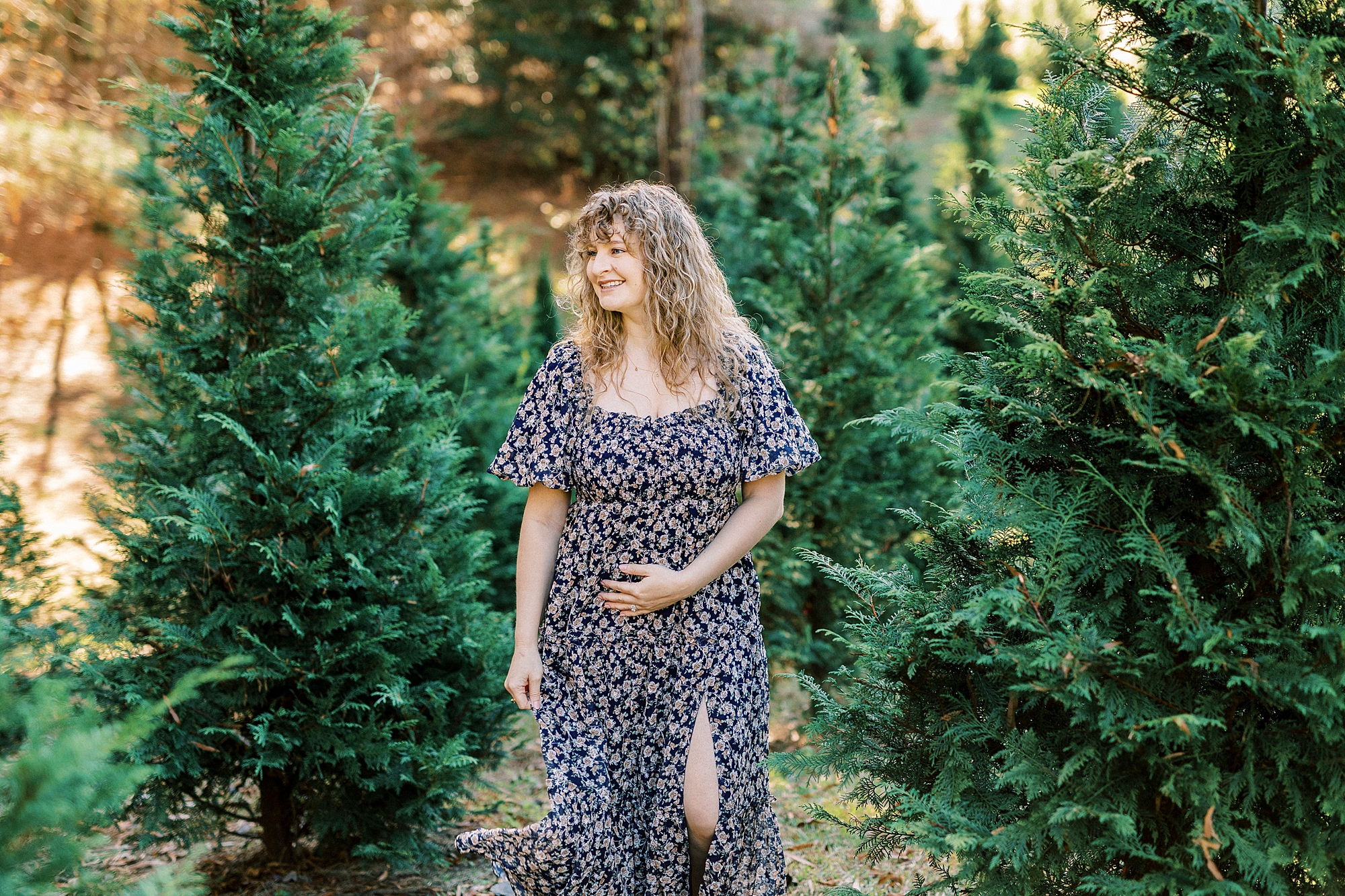 blonde woman holds tiny baby bump during NC Christmas tree farm