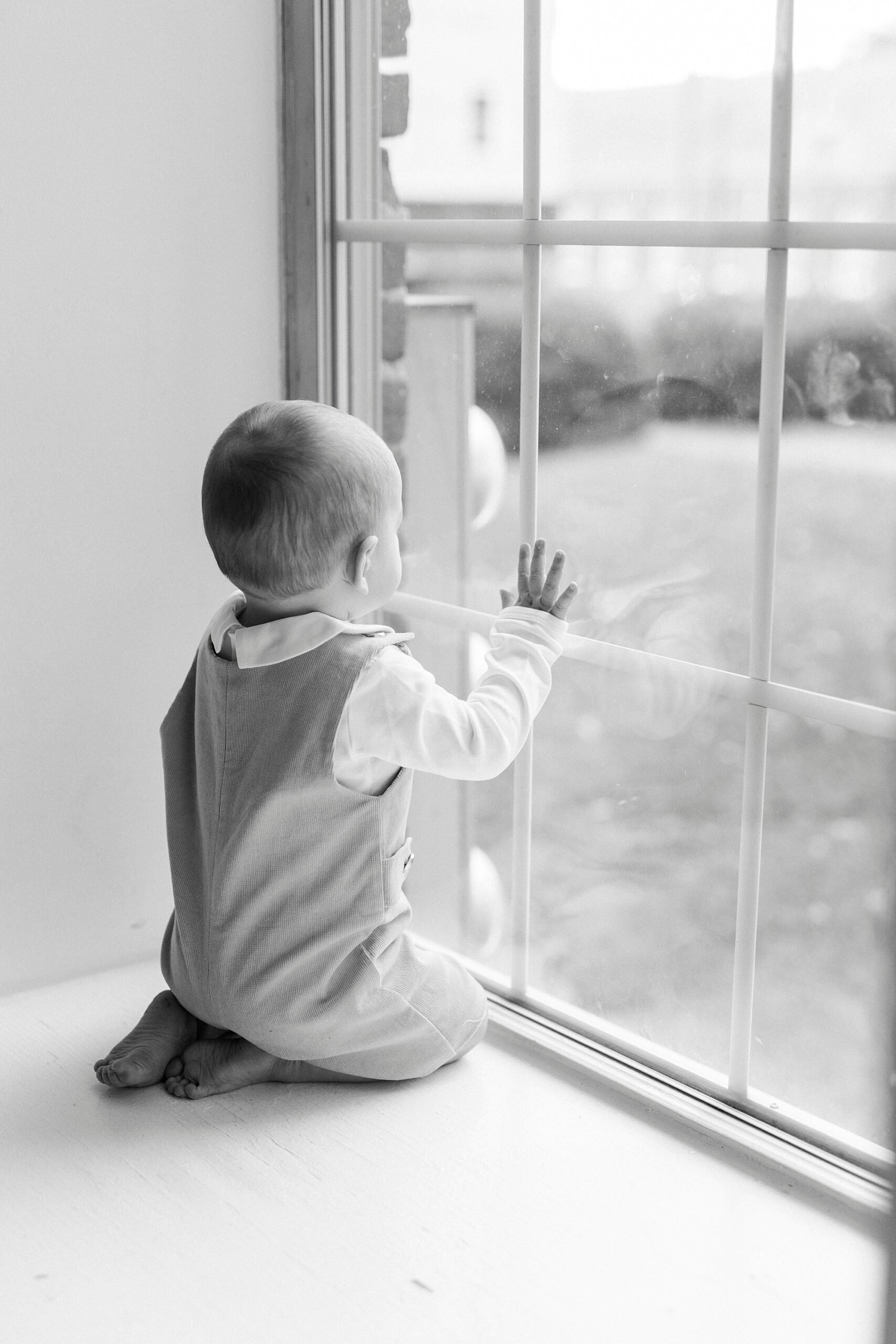 baby looks out window during first birthday photos in Concord NC studio