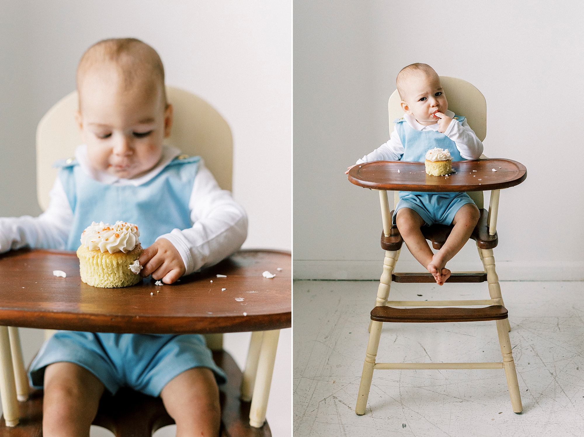 baby in blue romper picks at cupcake in wooden high chair during first birthday photos in Concord NC studio