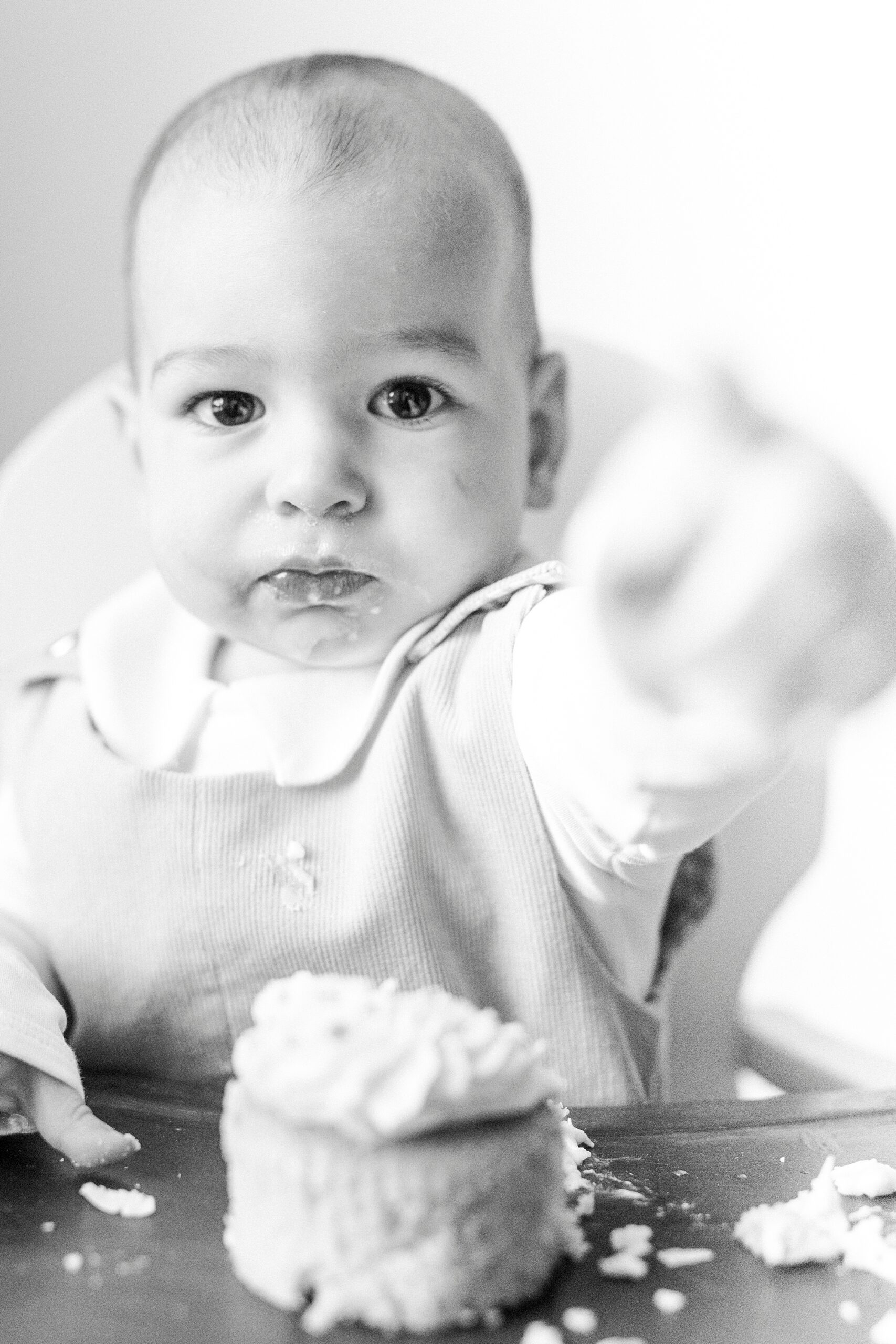 baby reaches out with icing on finger during first birthday photos in Concord NC studio