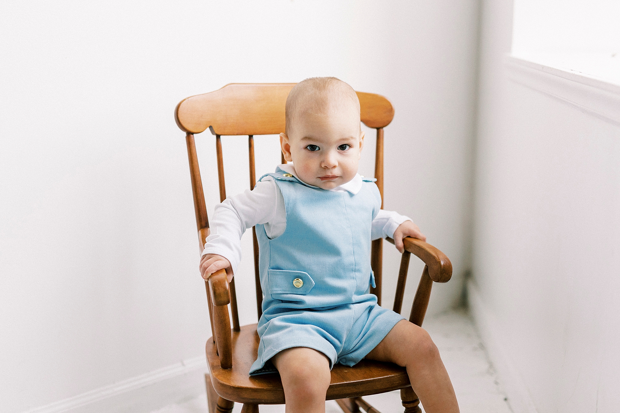 baby boy sits in wooden rocking chair in Concord NC studio for first birthday photos