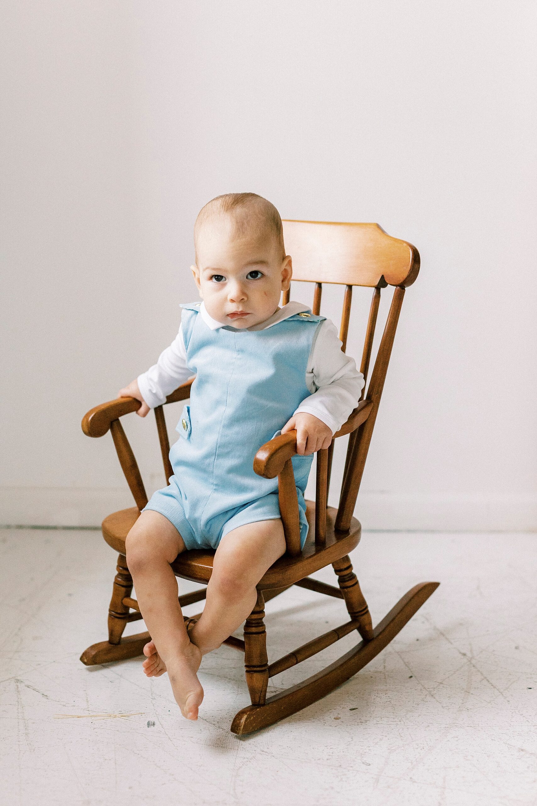baby boy rocks in wooden chair during first birthday photos in Concord NC studio