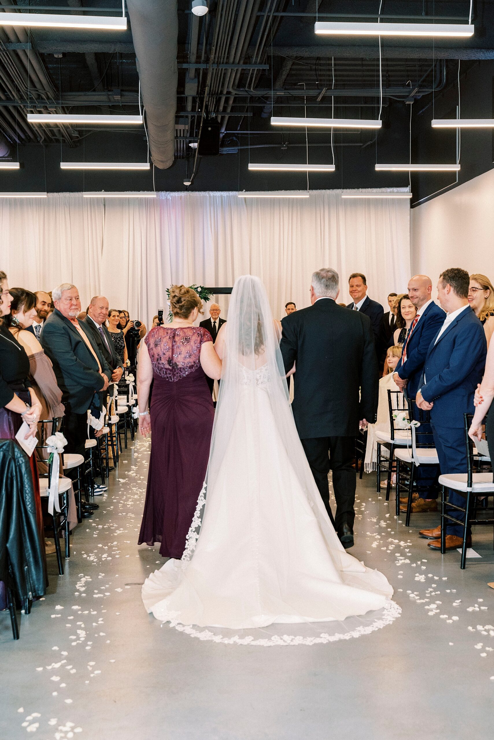parents escort bride down aisle during ceremony inside the Mint Museum Uptown
