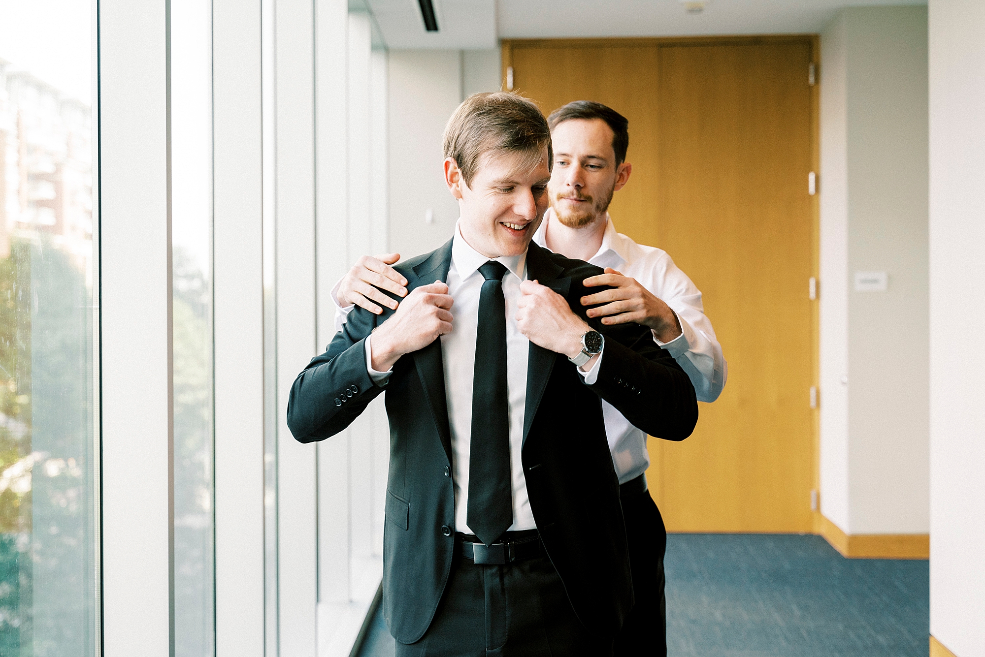 groomsmen helps groom into jacket inside the Mint Museum Uptown