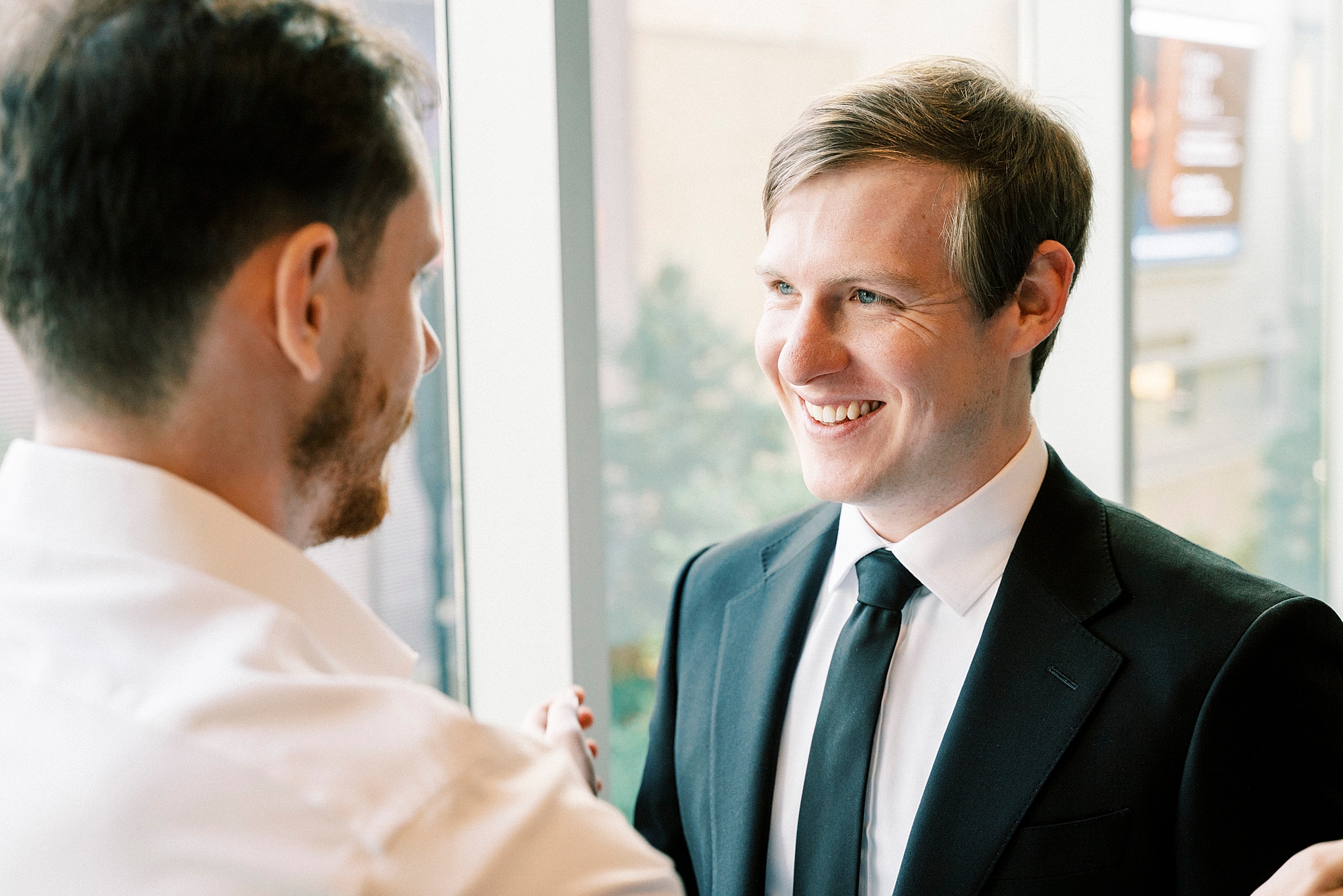 groomsman smiles at groom during prep inside the Mint Museum Uptown