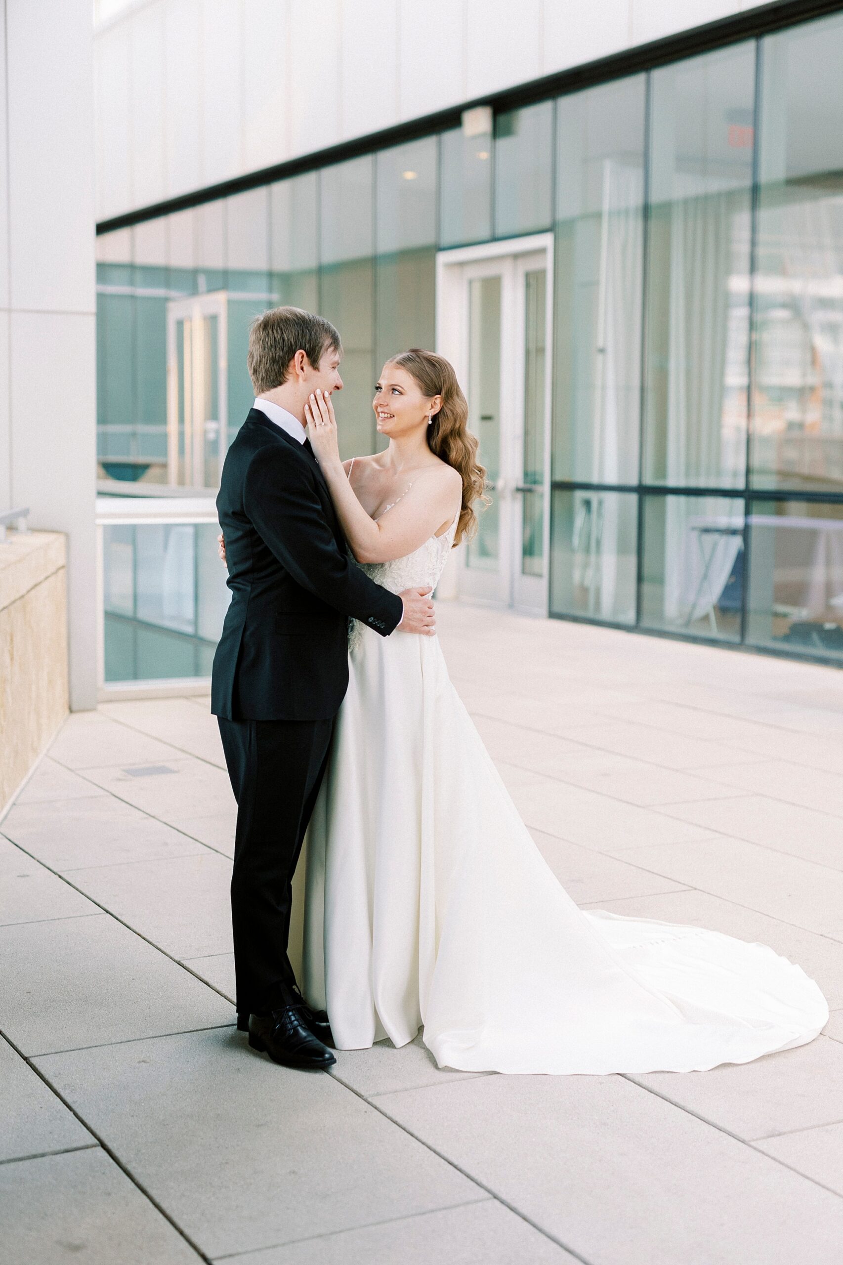 newlyweds hug inside the Mint Museum Uptown in front of glass windows