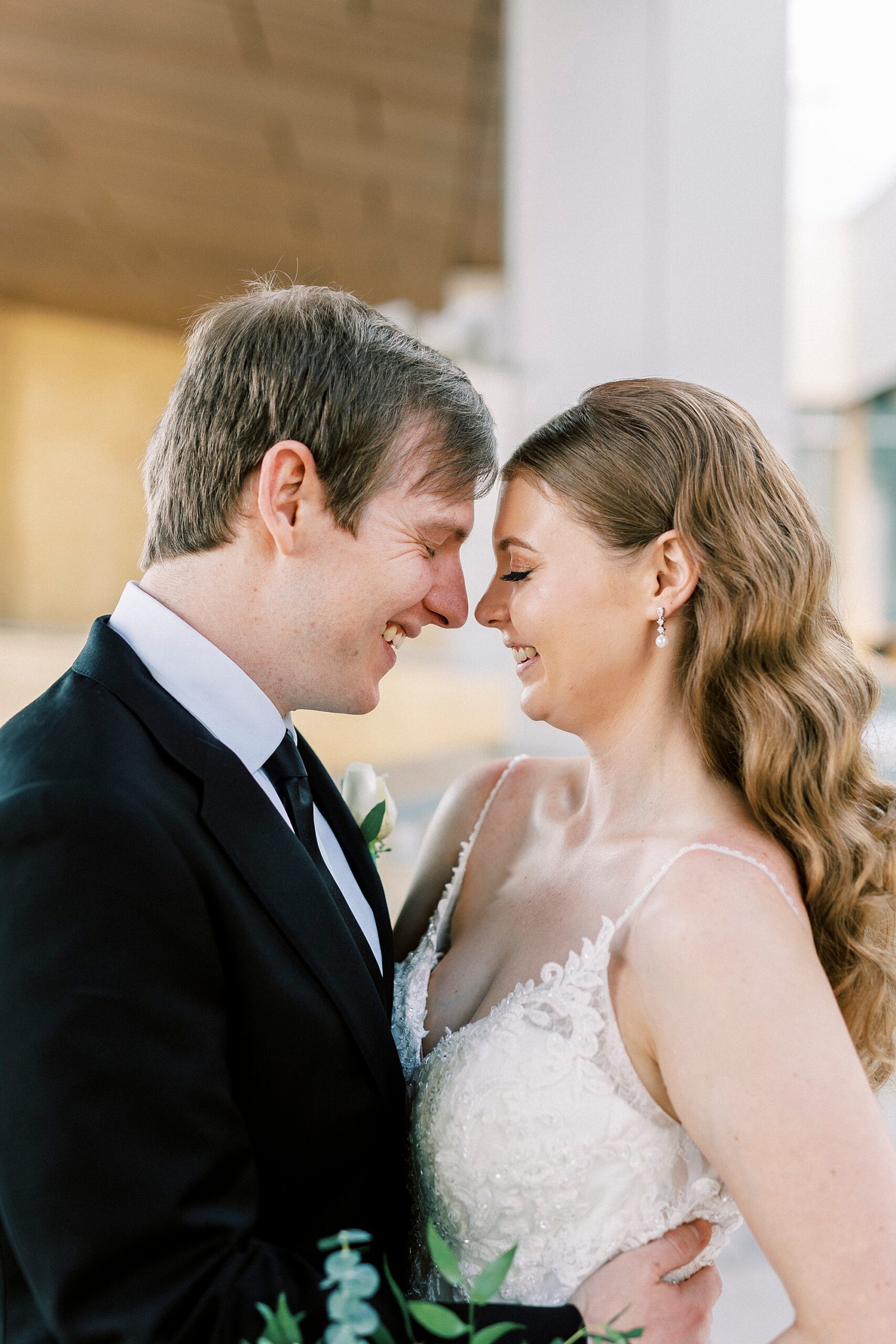 bride and groom smile leaning heads together outside the Mint Museum Uptown