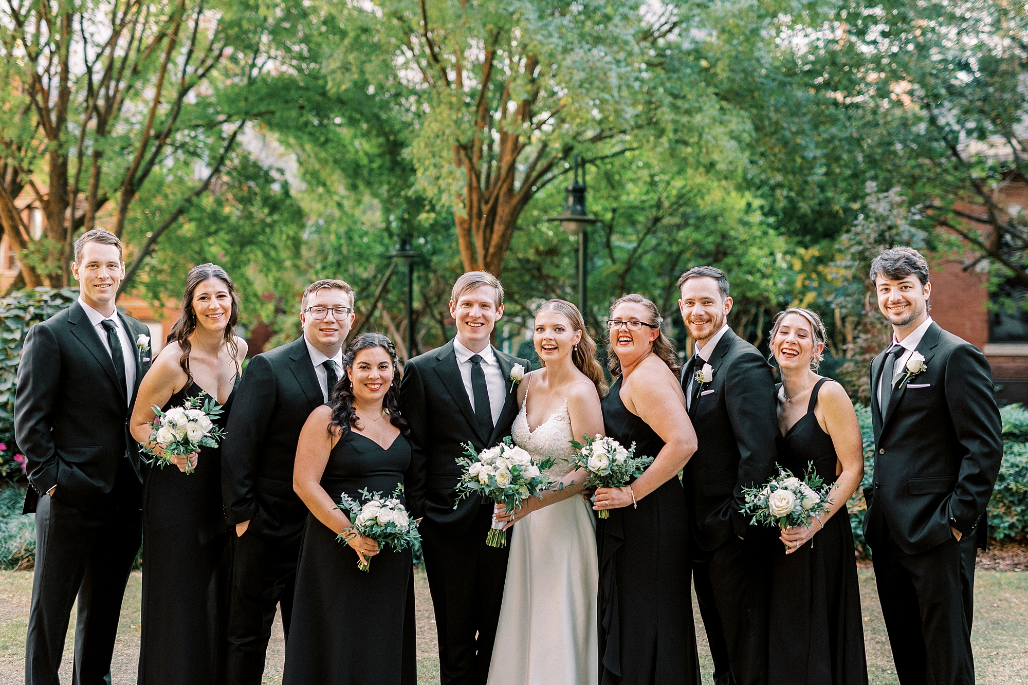 newlyweds pose with wedding party in all black attire in Charlotte park