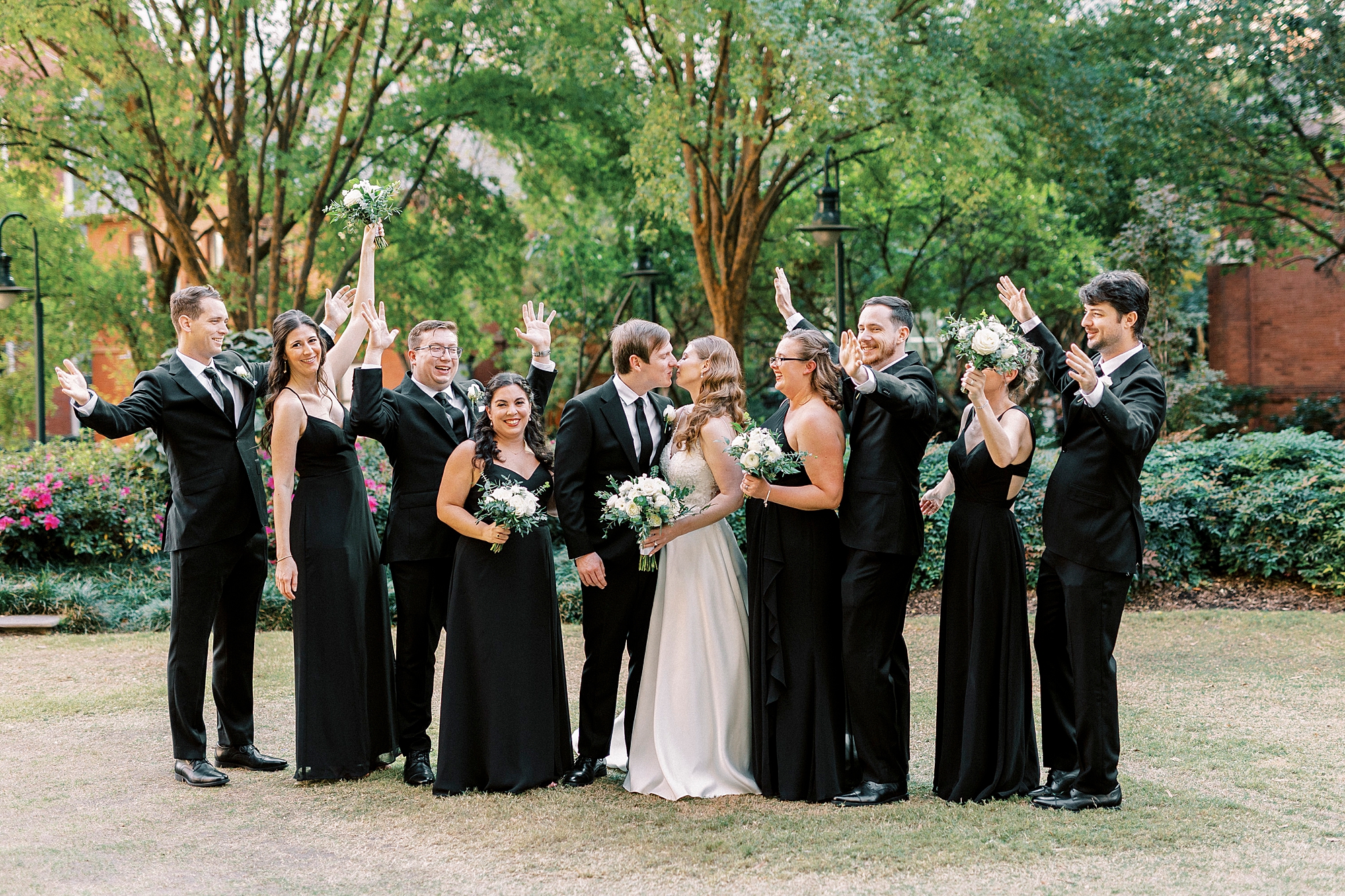 bride and groom kiss with wedding party cheering around them