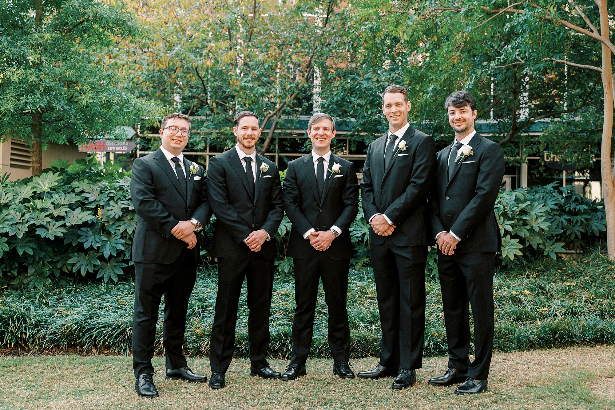 groom stands with groomsmen in gardens outside the Mint Museum Uptown