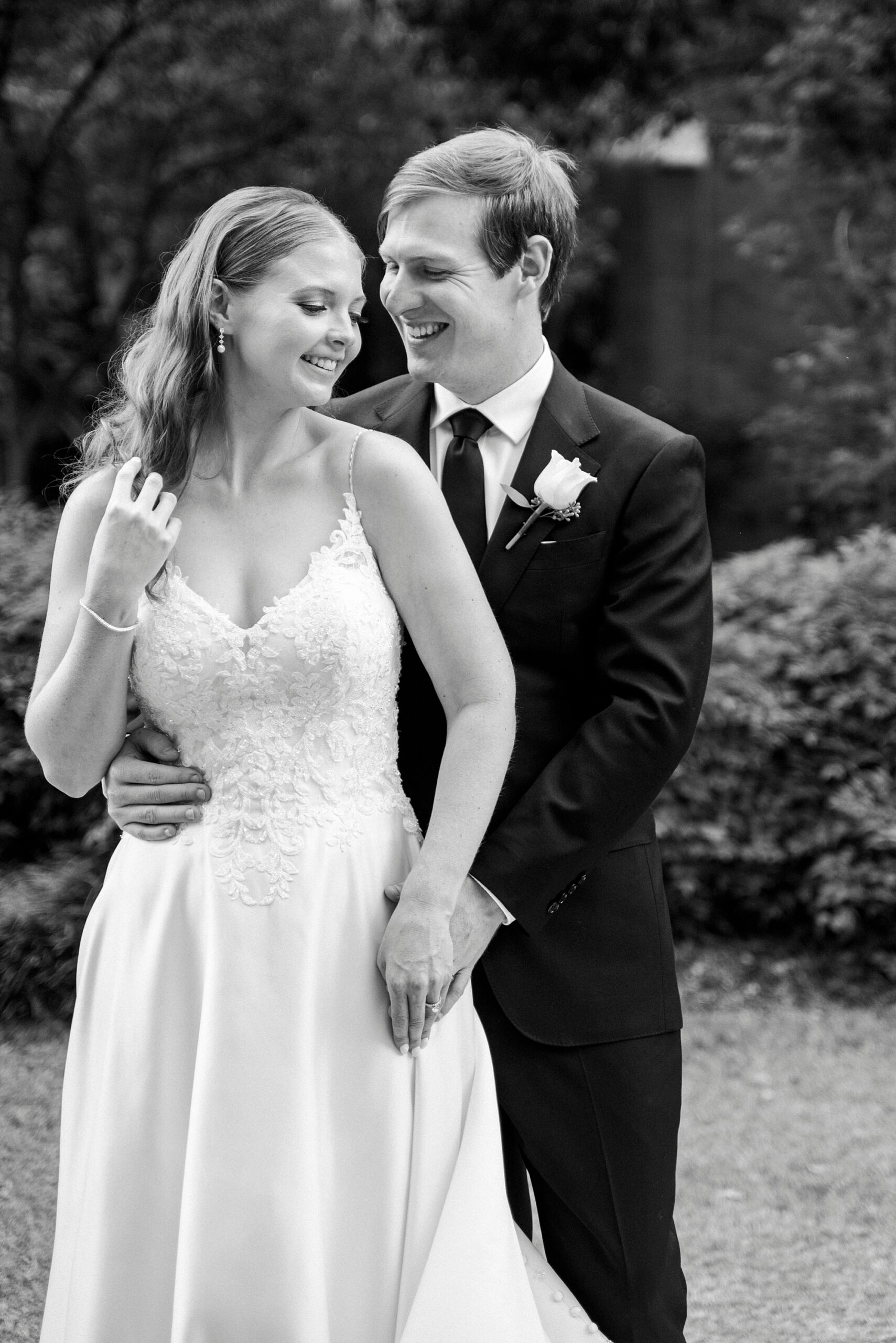 groom hugs bride from behind in garden at the Mint Museum Uptown