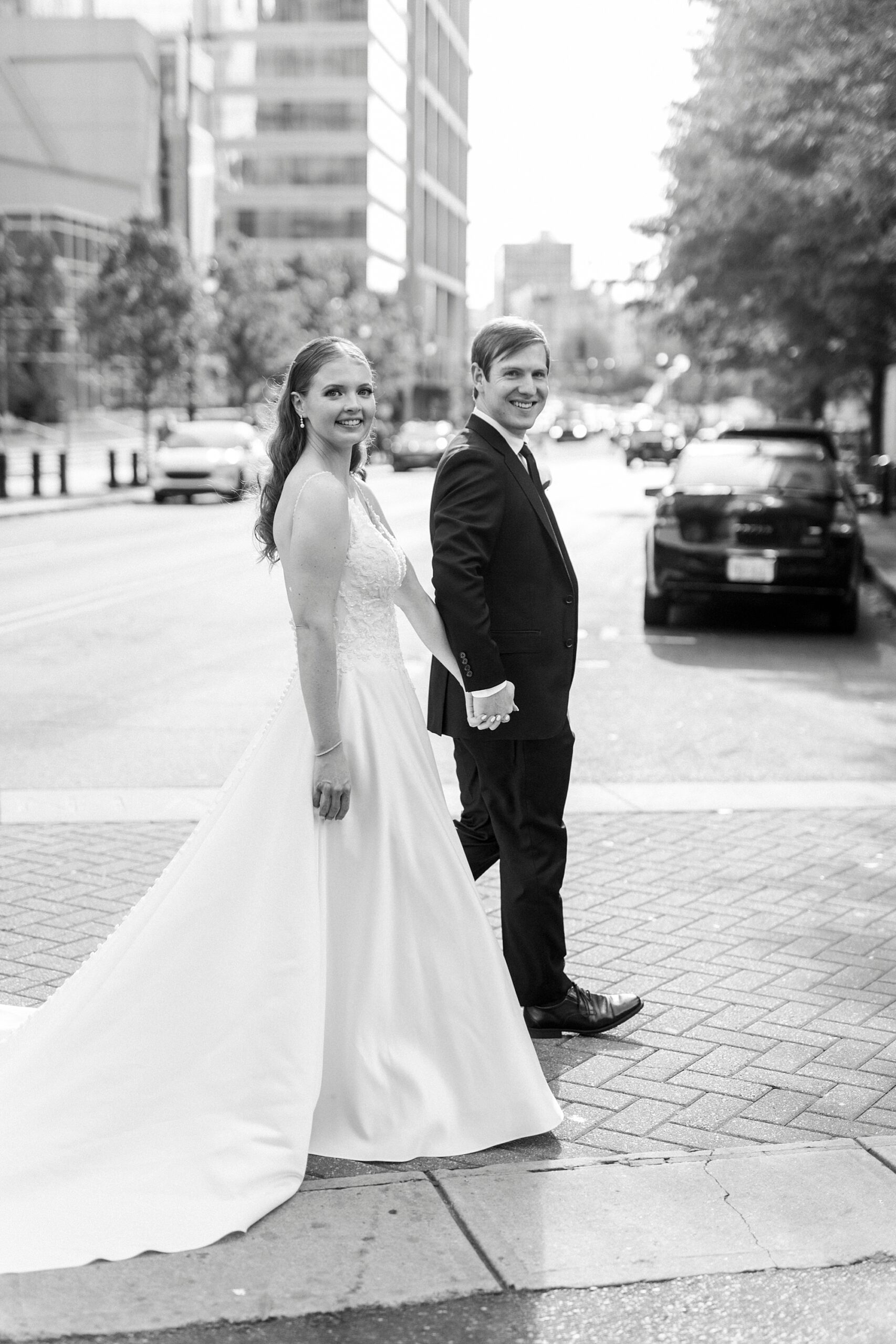 bride and groom hold hands walking on street outside the Mint Museum Uptown