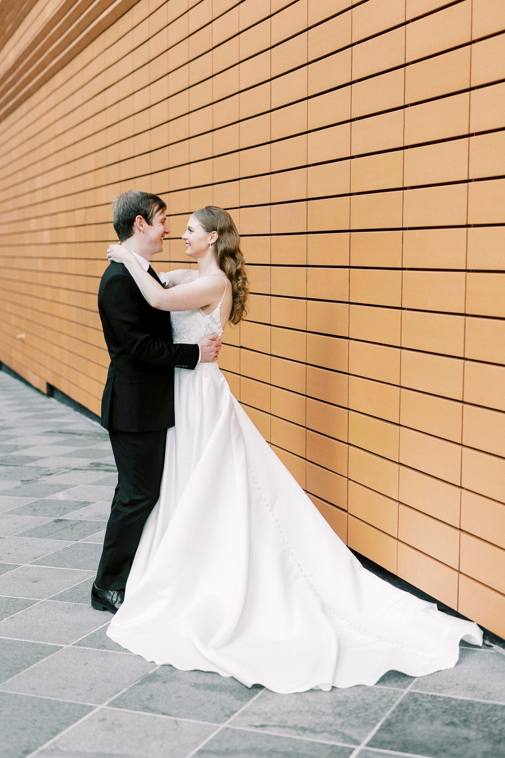 bride and groom smile in front or orange wall at the Mint Museum Uptown