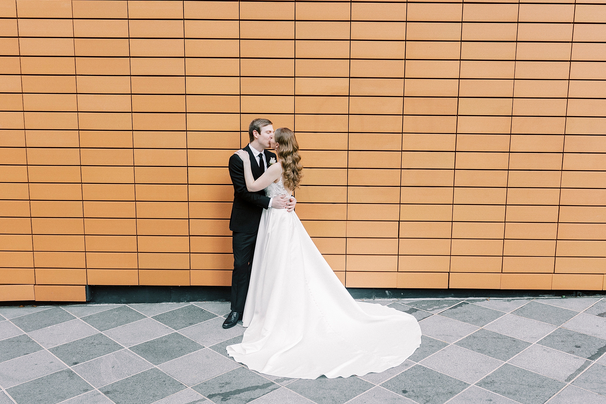 newlyweds kiss by orange wall at the Mint Museum Uptown