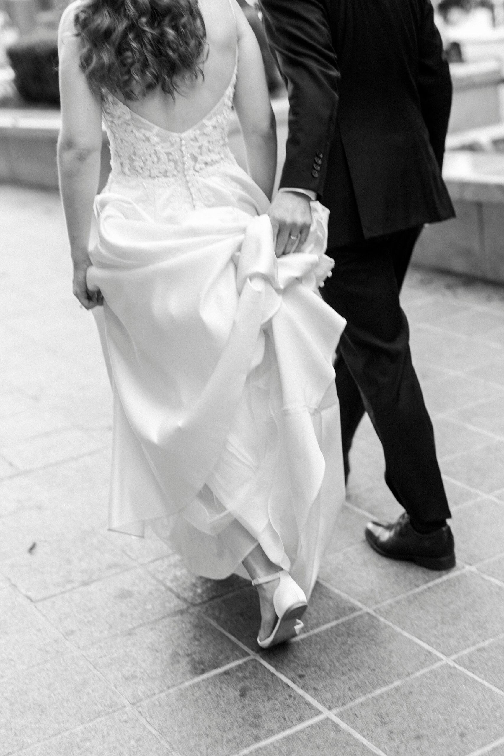groom helps bride carry wedding dress skirt on street