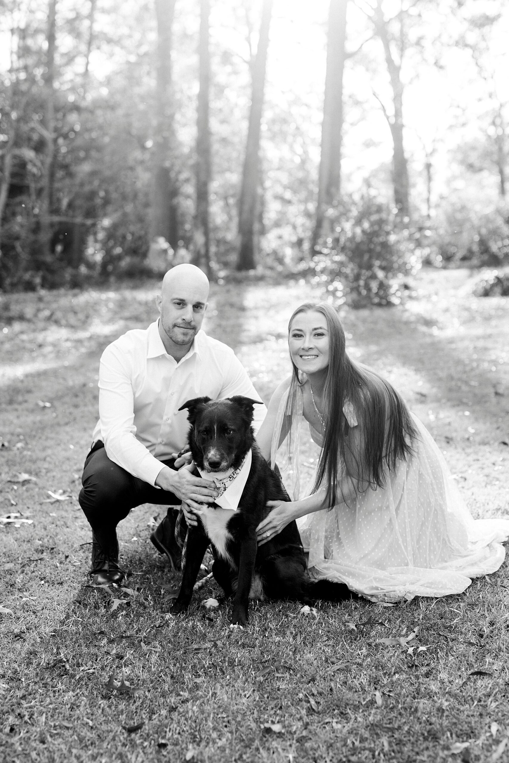 engaged couple kneels down with black dog during engagement session at Glencairn Garden