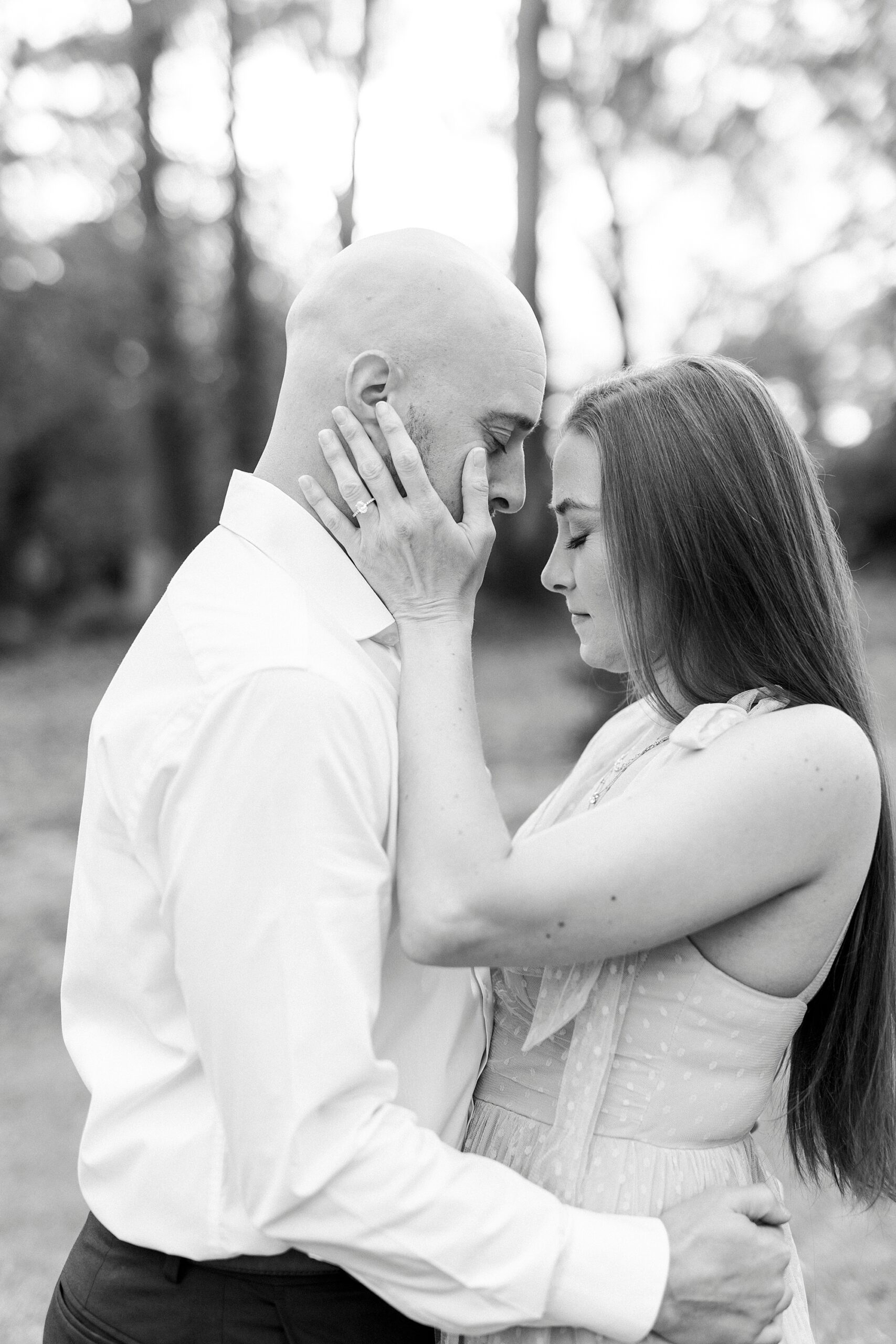 man leans head into woman's forehead during summer engagement photos at Glencairn Garden