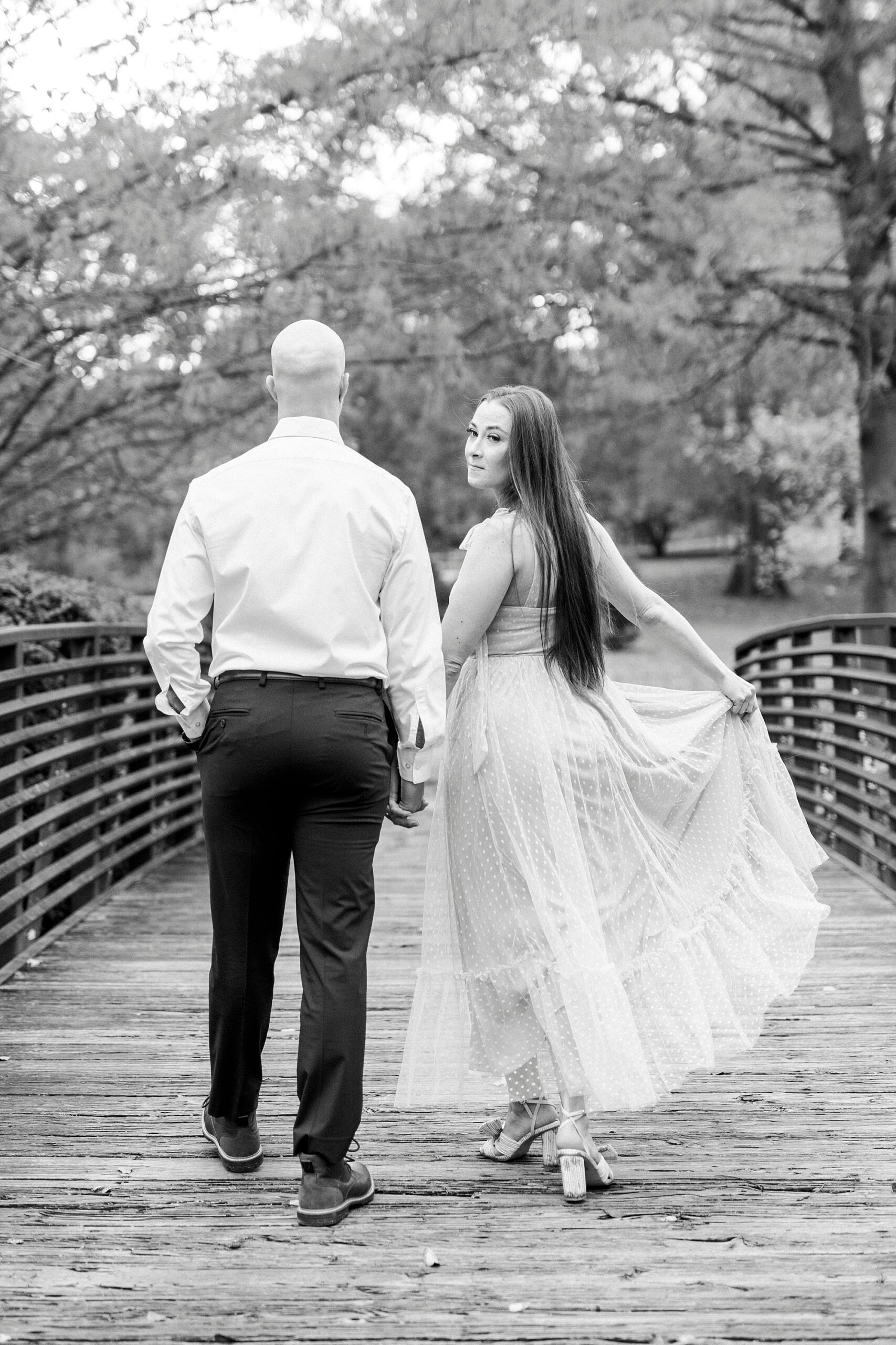 woman holds out skirt on her dress walking over wooden bridge at Glencairn Garden