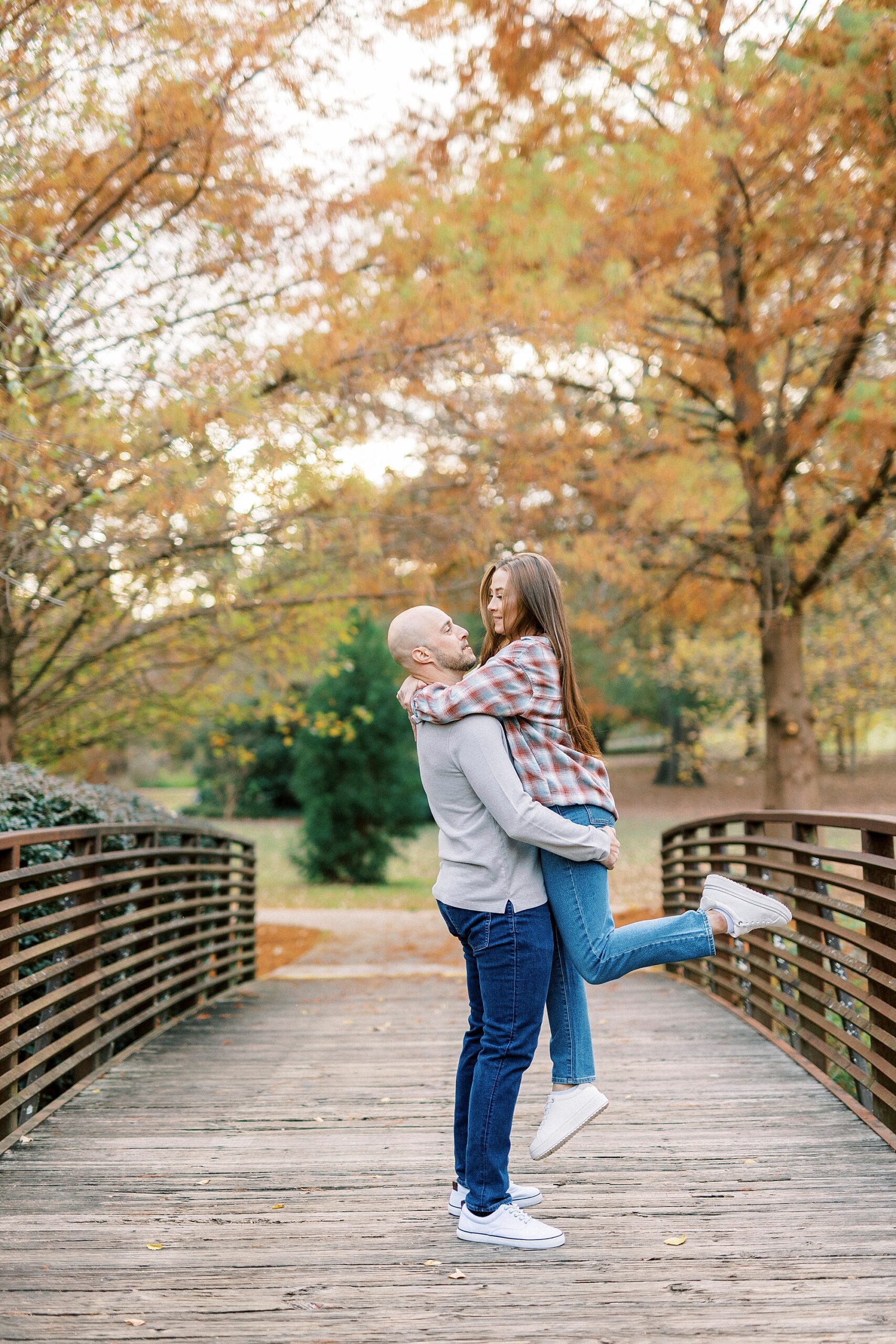 man lifts up woman on wooden bridge in flannel shirt