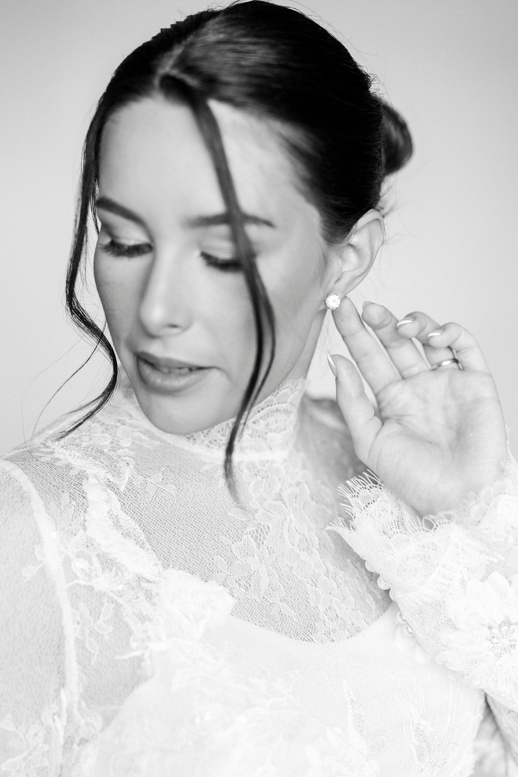 bride with high end fashion hair style holds pearl earring looking down
