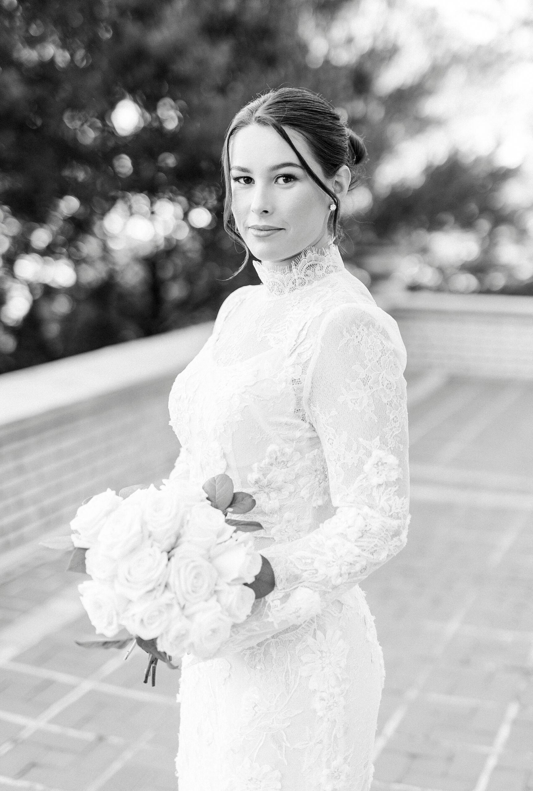 bride in high neck wedding gown holds bouquet of white flowers on patio