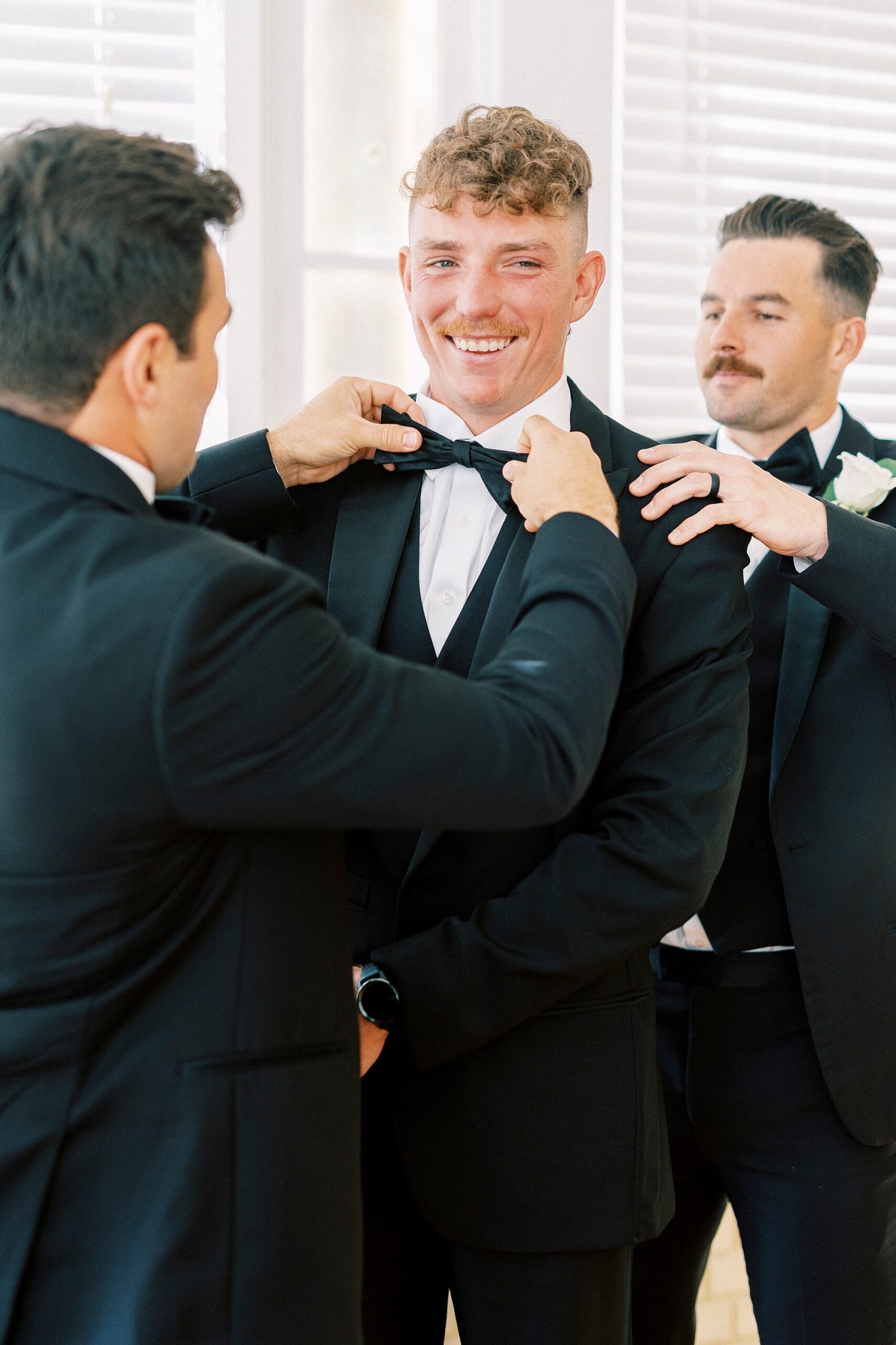 groomsman adjusts bowtie for groom during prep at Separk Mansion