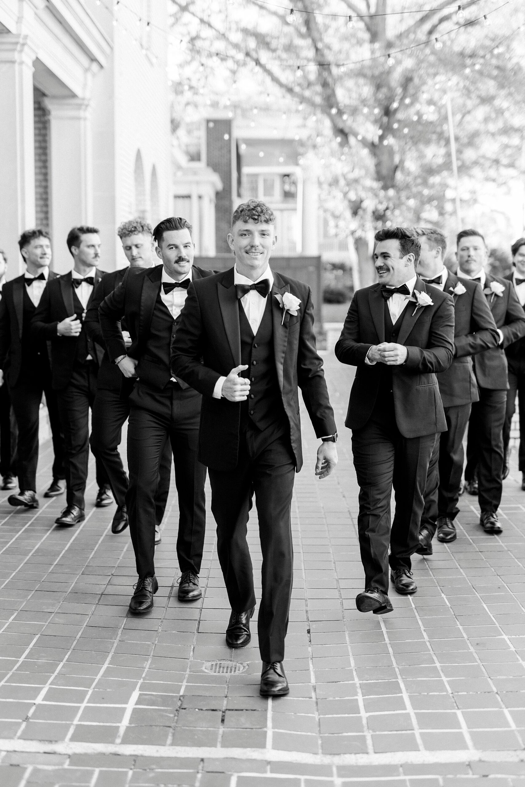 groom and groomsmen walk on patio in black tuxes