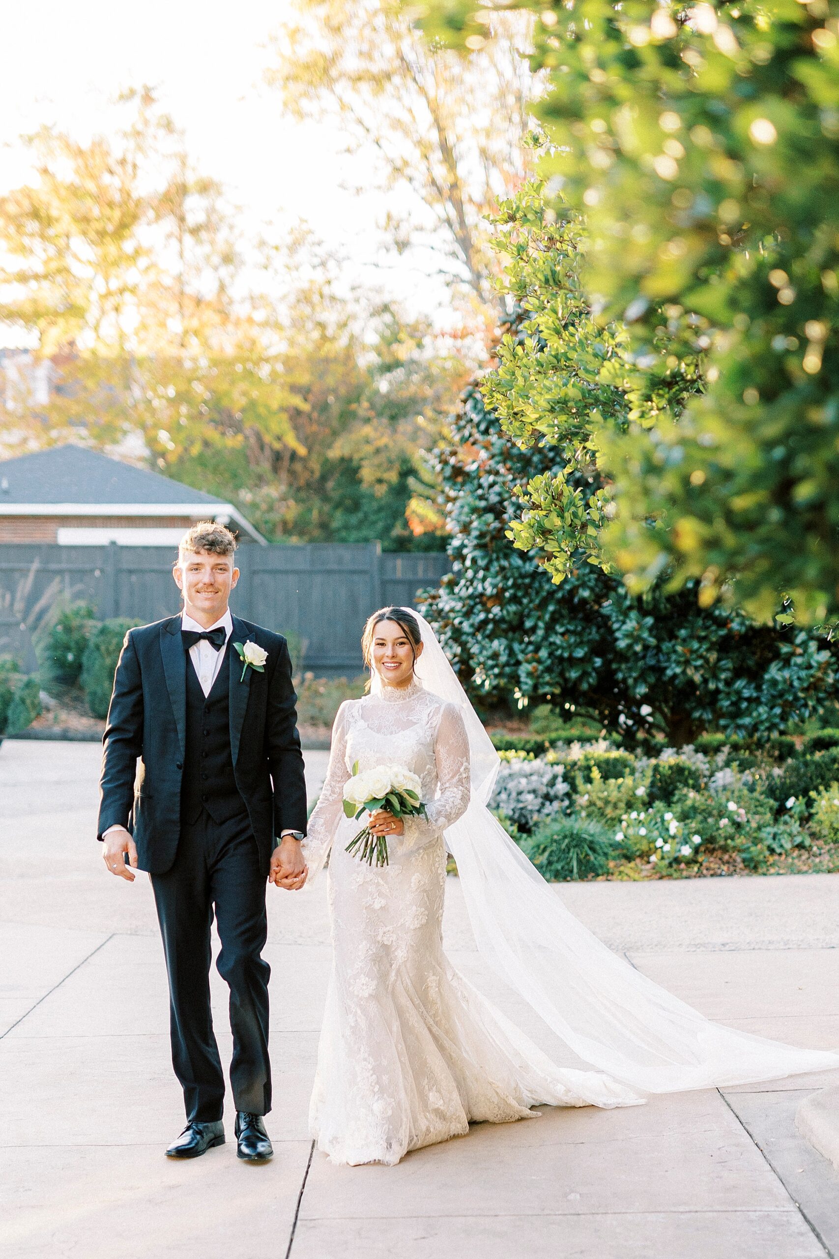 bride and groom hold hands in front of trees at Separk Mansion with sun coming through garden
