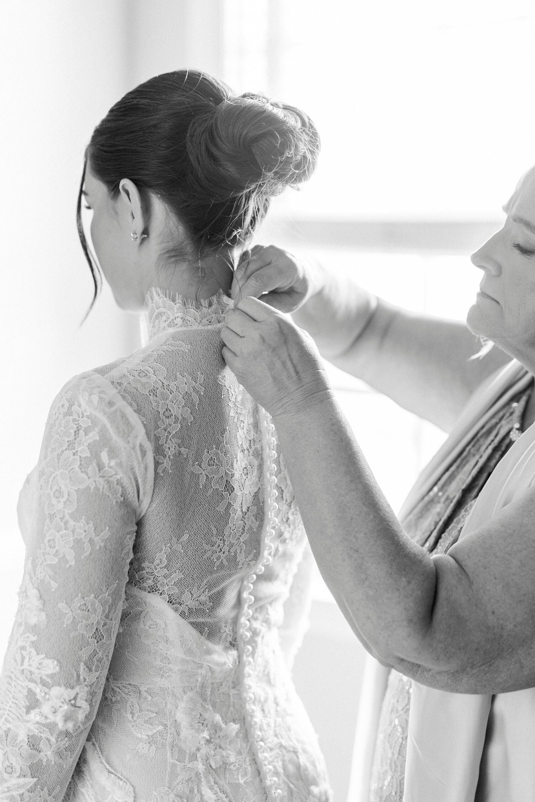 woman buttons up lace back of wedding gown