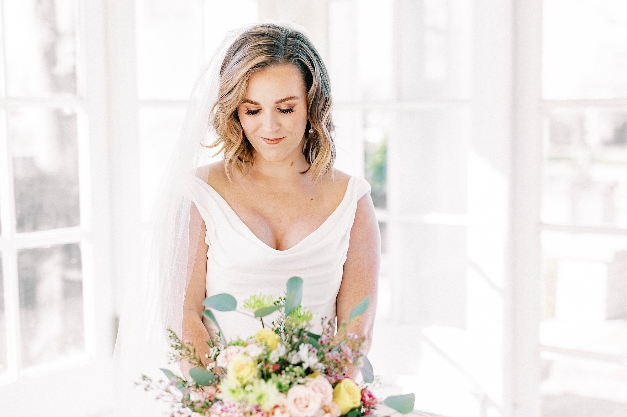 bride looks down at colorful bouquet in Justin Alexander gown