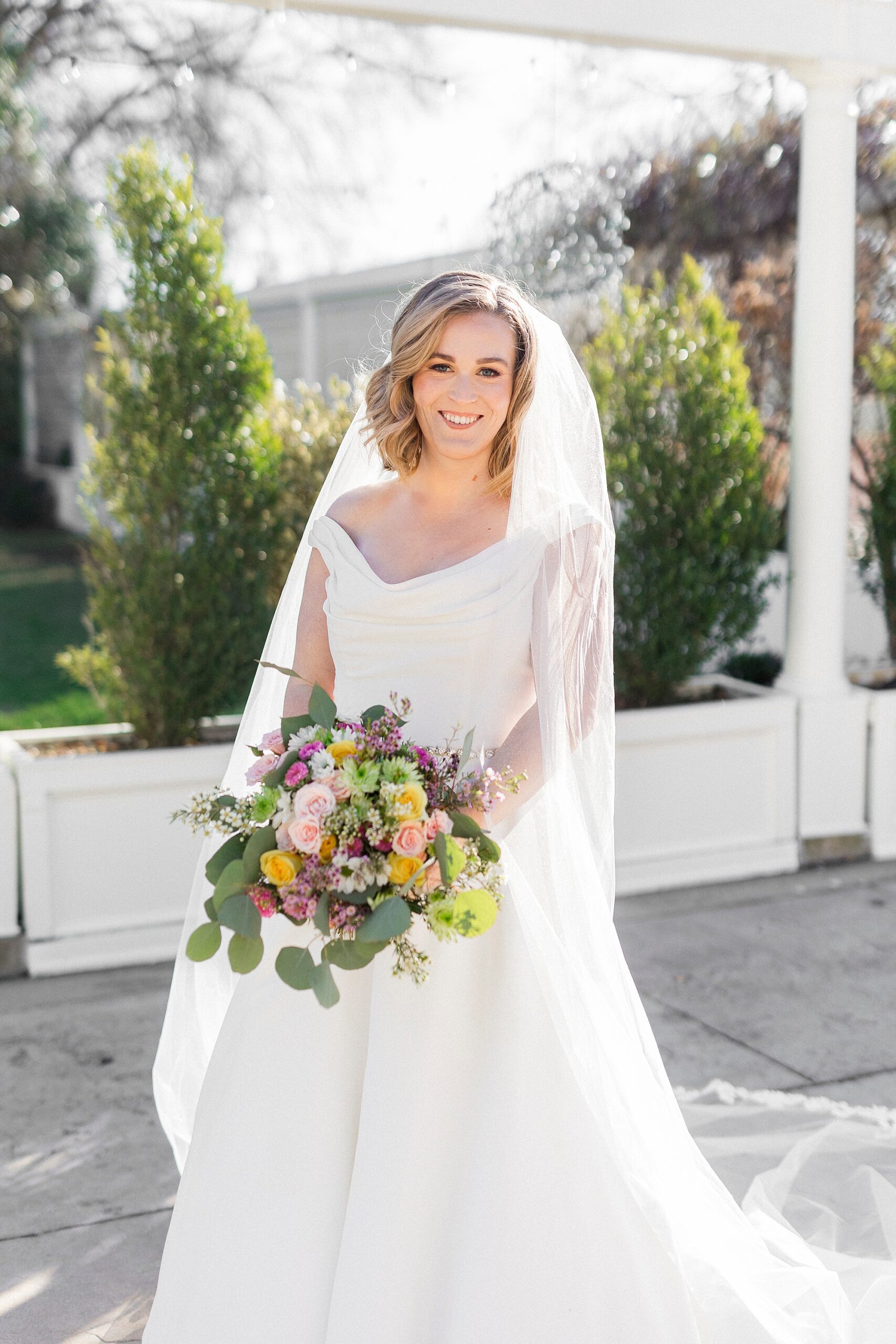 bride holds colorful bouquet standing in Justin Alexander wedding gown