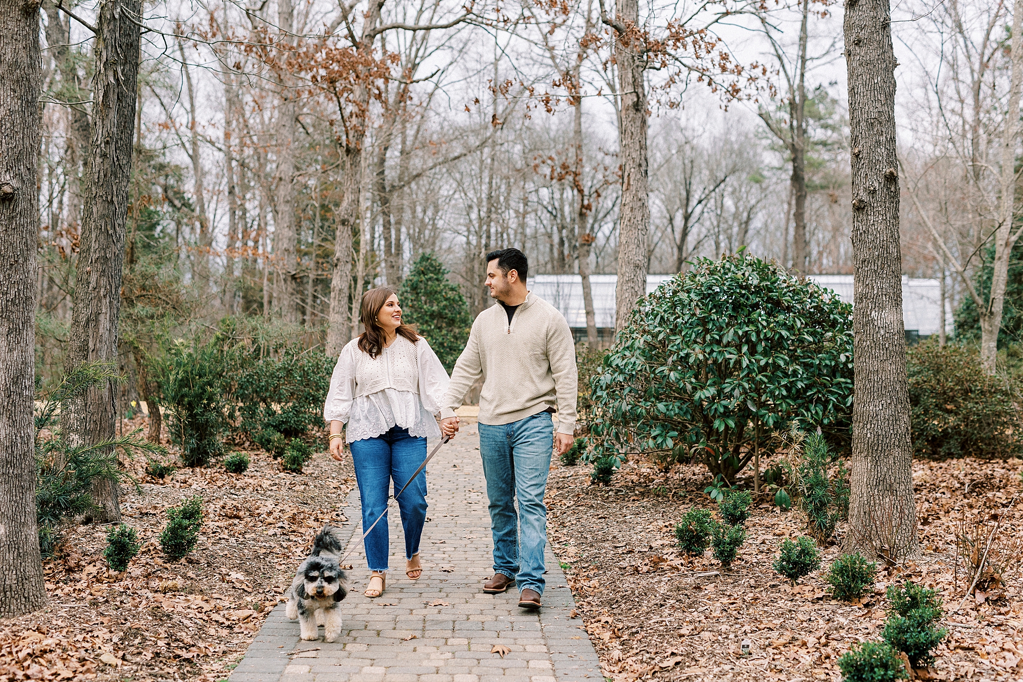 couple holds hands walking through pathway at Morning Glory Farm with dog
