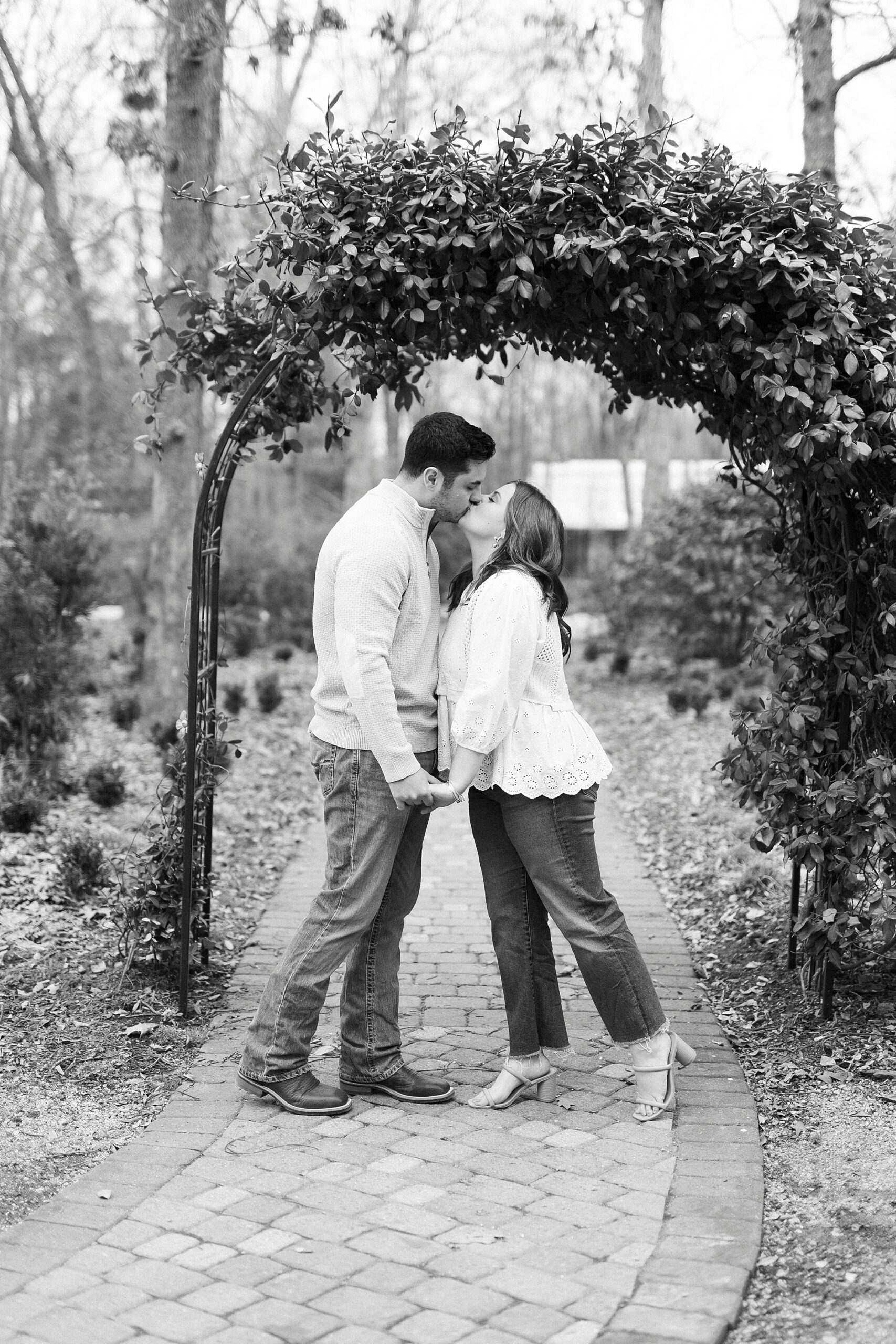 couple leans to kiss under arbor covered in leaves