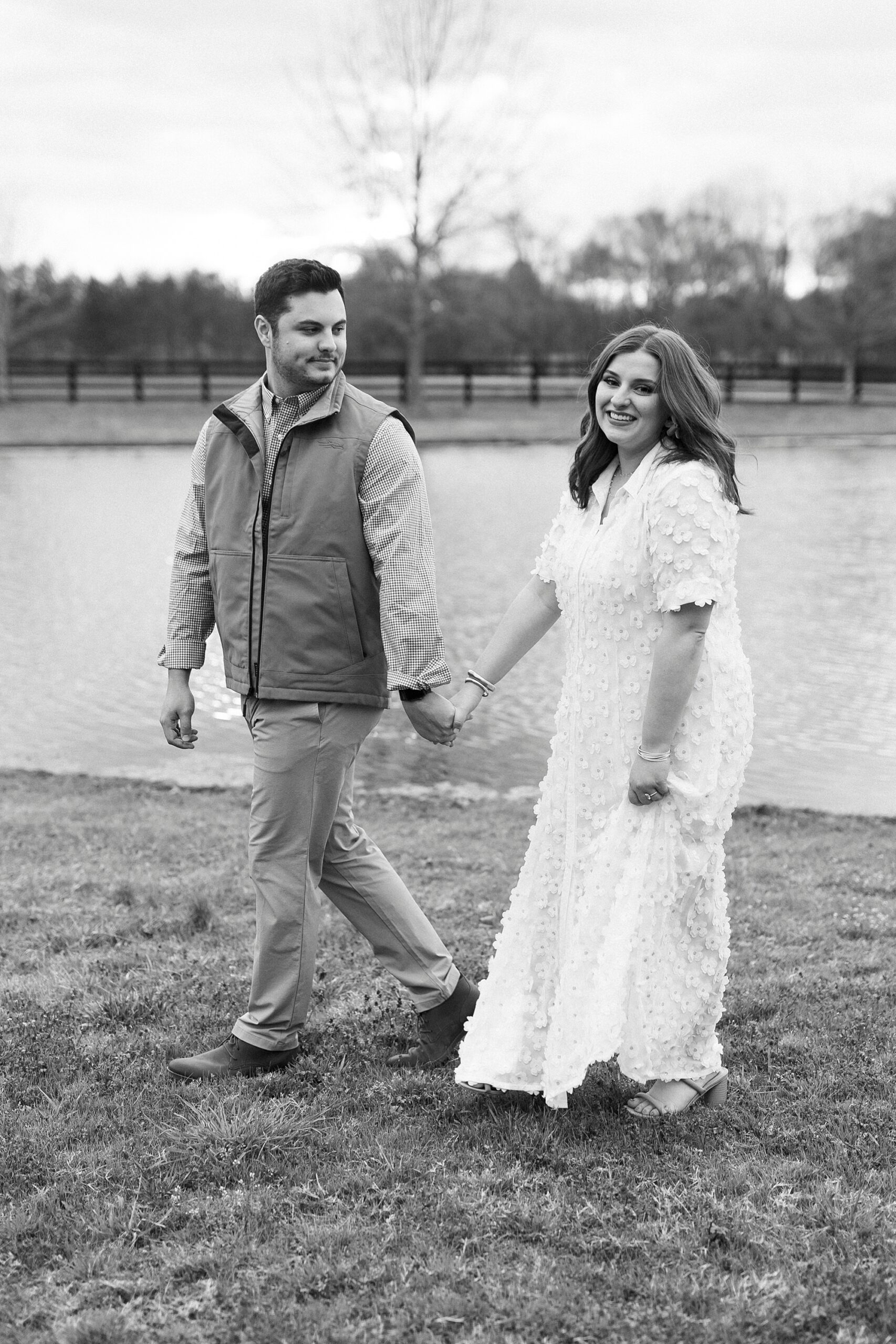couple holds hands walking by pond during engagement session at Morning Glory Farm