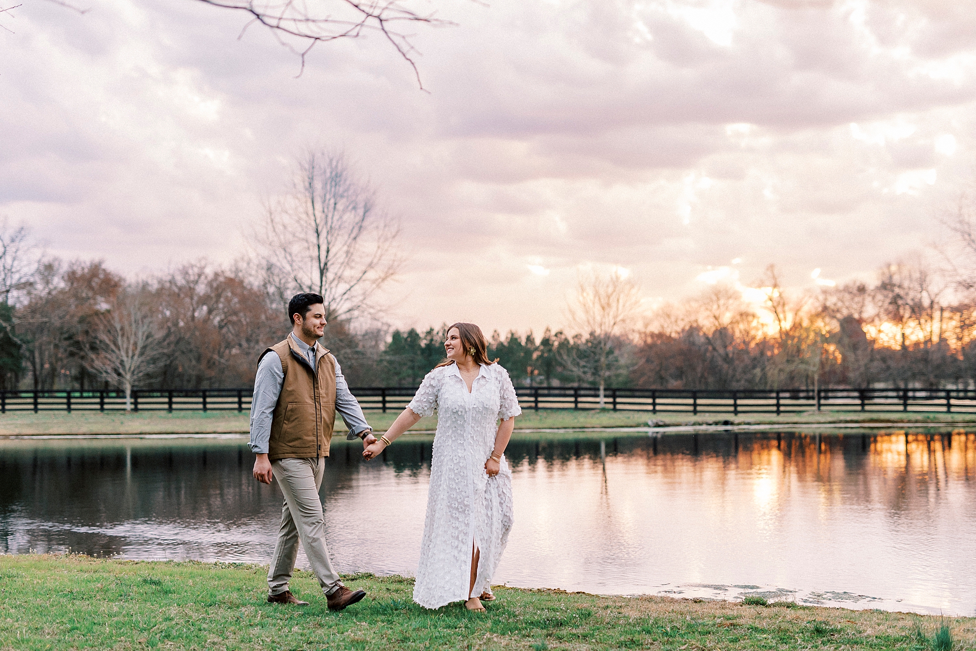 woman in white dress holds hands with man walking next to pond at sunset at Morning Glory Farm